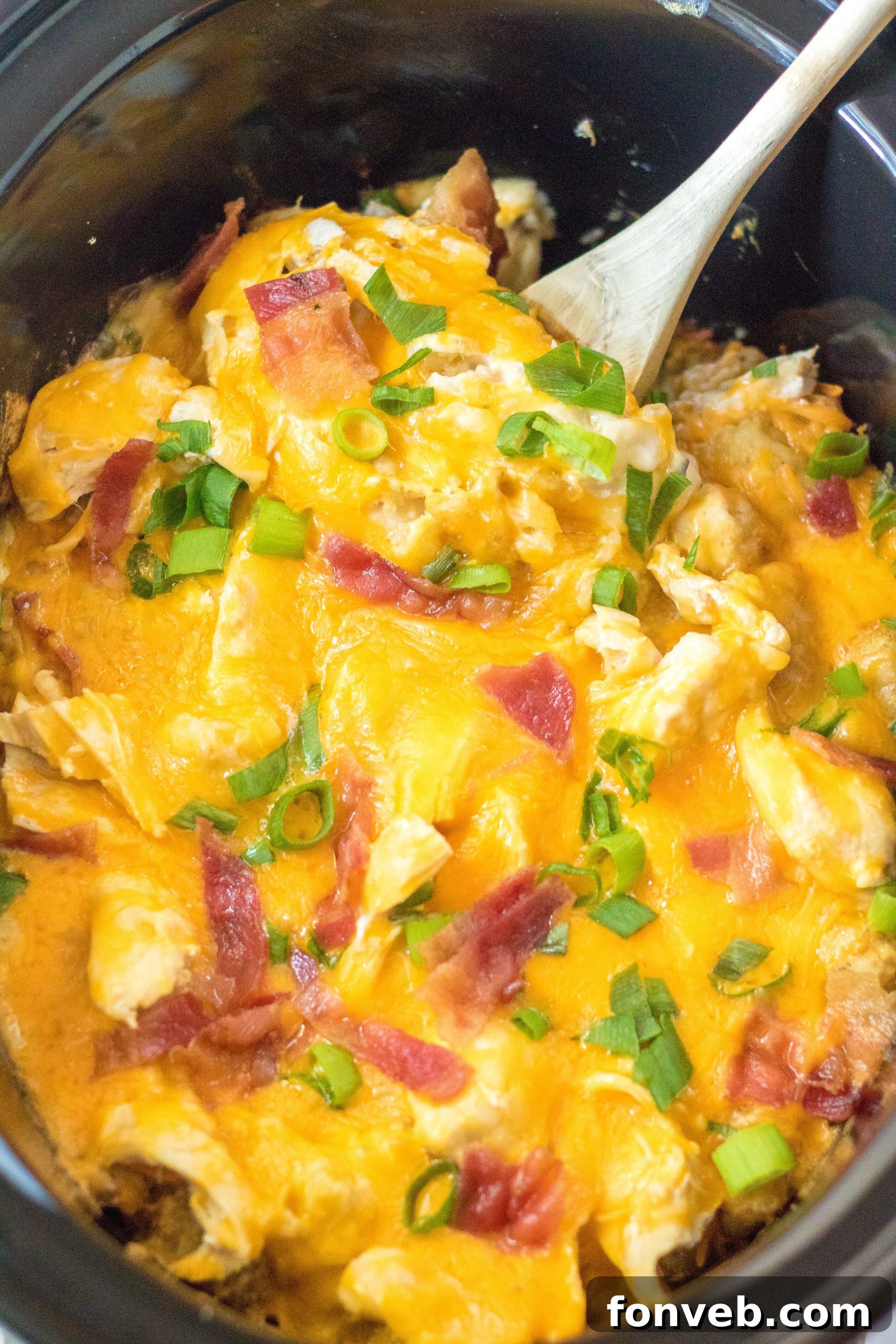 Tater Tot Casserole in the crock pot with a spoon ready to scoop, rich and creamy