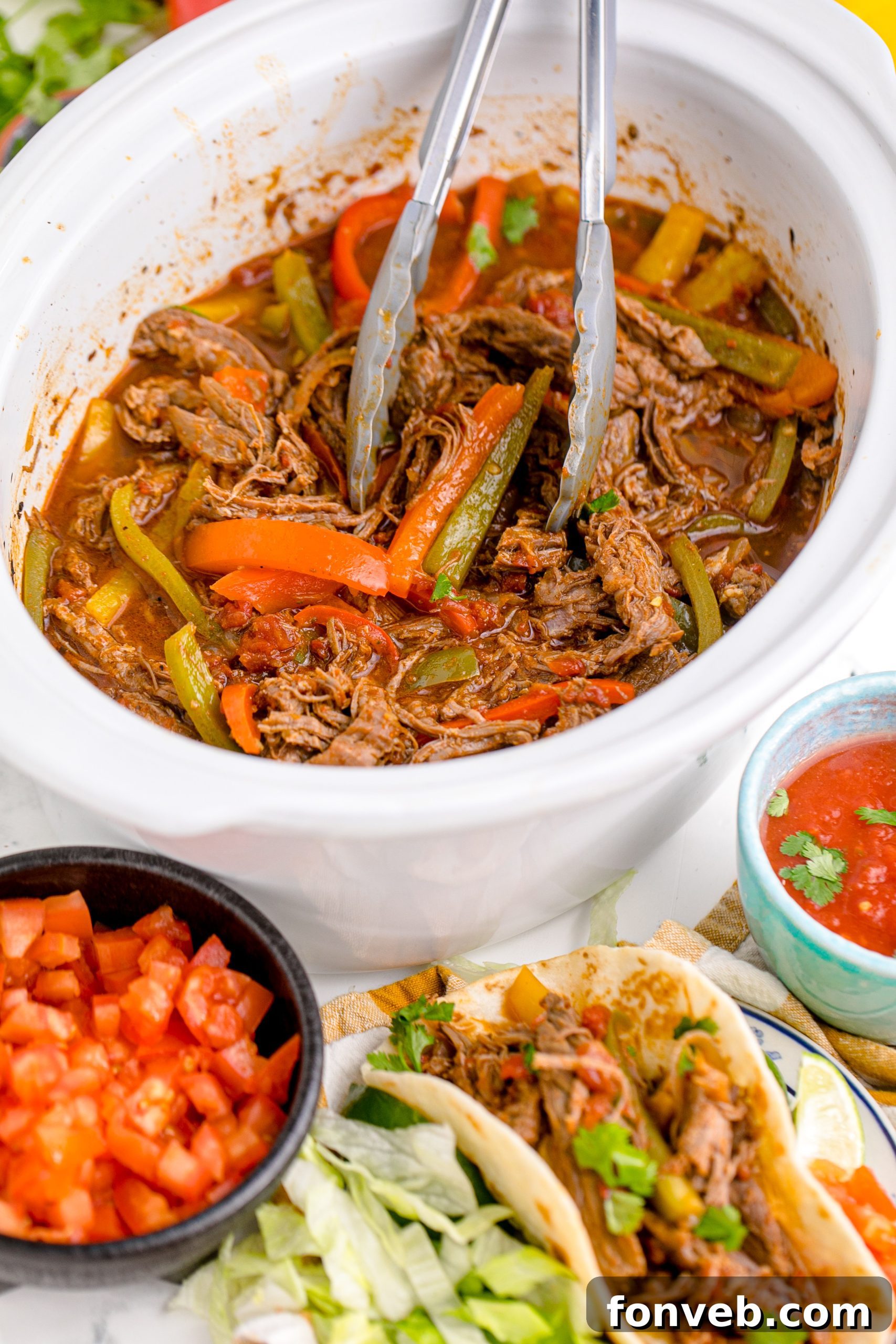 Steak Fajitas in a crock pot with tongs lifting the steak, with a bowl of salasa next to it