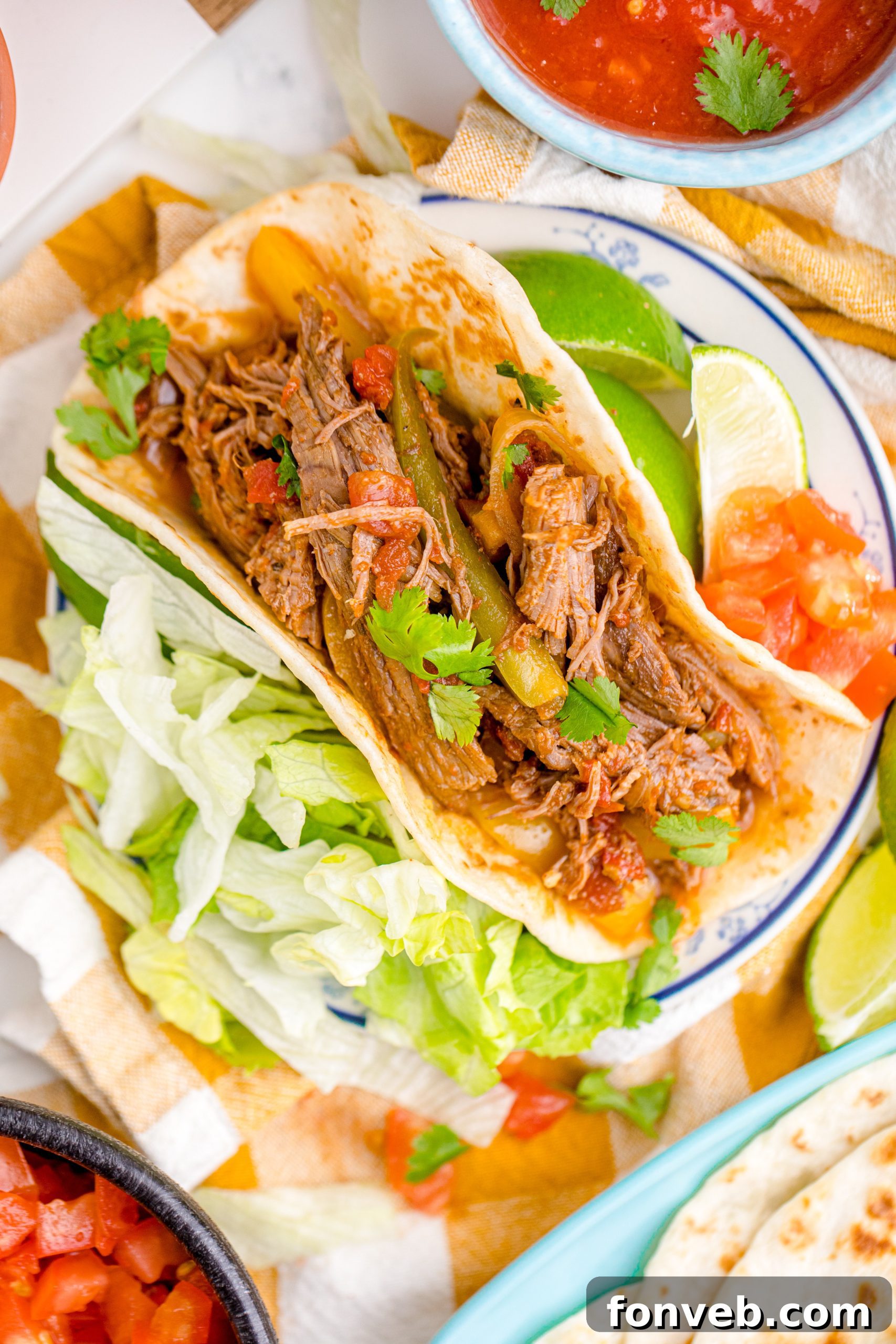 Steak Fajitas wrapped in a tortilla with lettuce piled next to it and limes with salsa