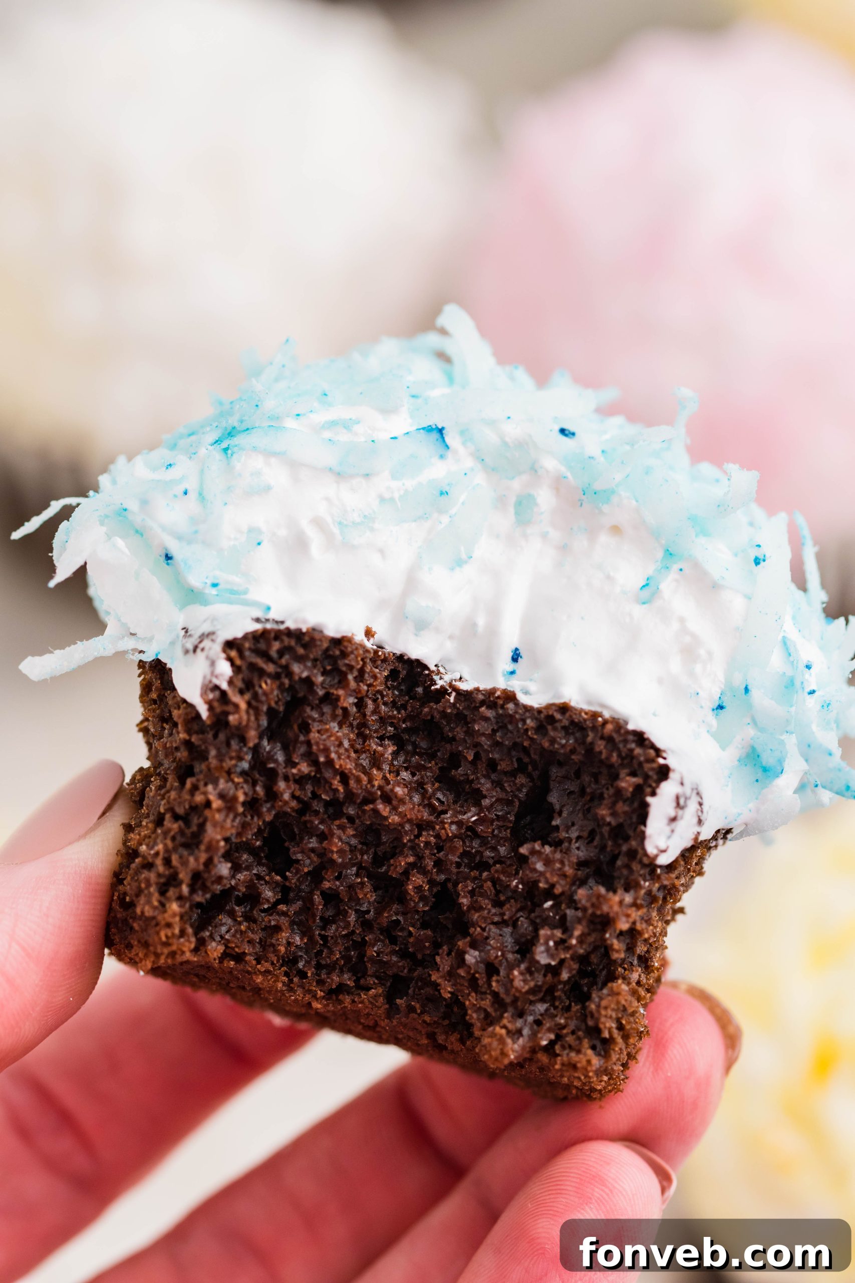 Chocolate cupcake with blue coconut shavings, marshmallow frosting with a bite taken out of it