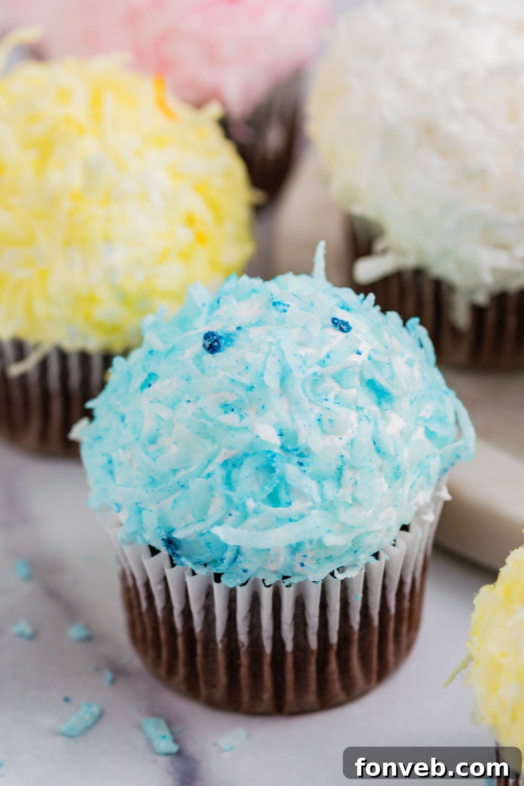 Assortment of pink, yellow, white, and blue chocolate cupcakes topped with coconut