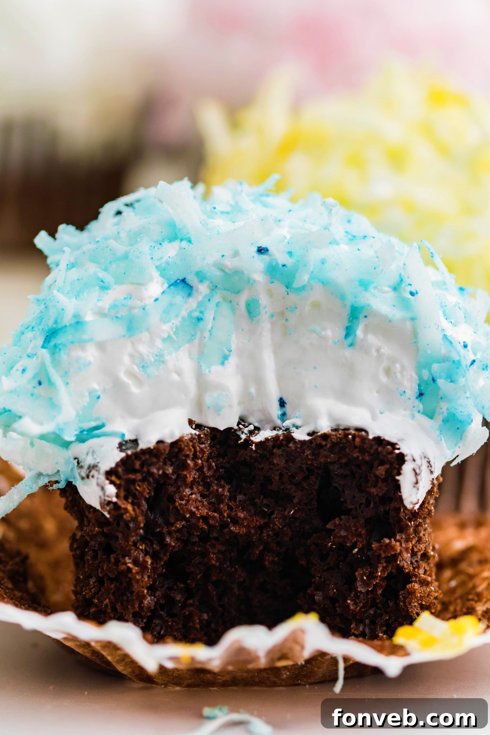 Chocolate cupcake with blue coconut shavings, marshmallow frosting with a bite taken out of it