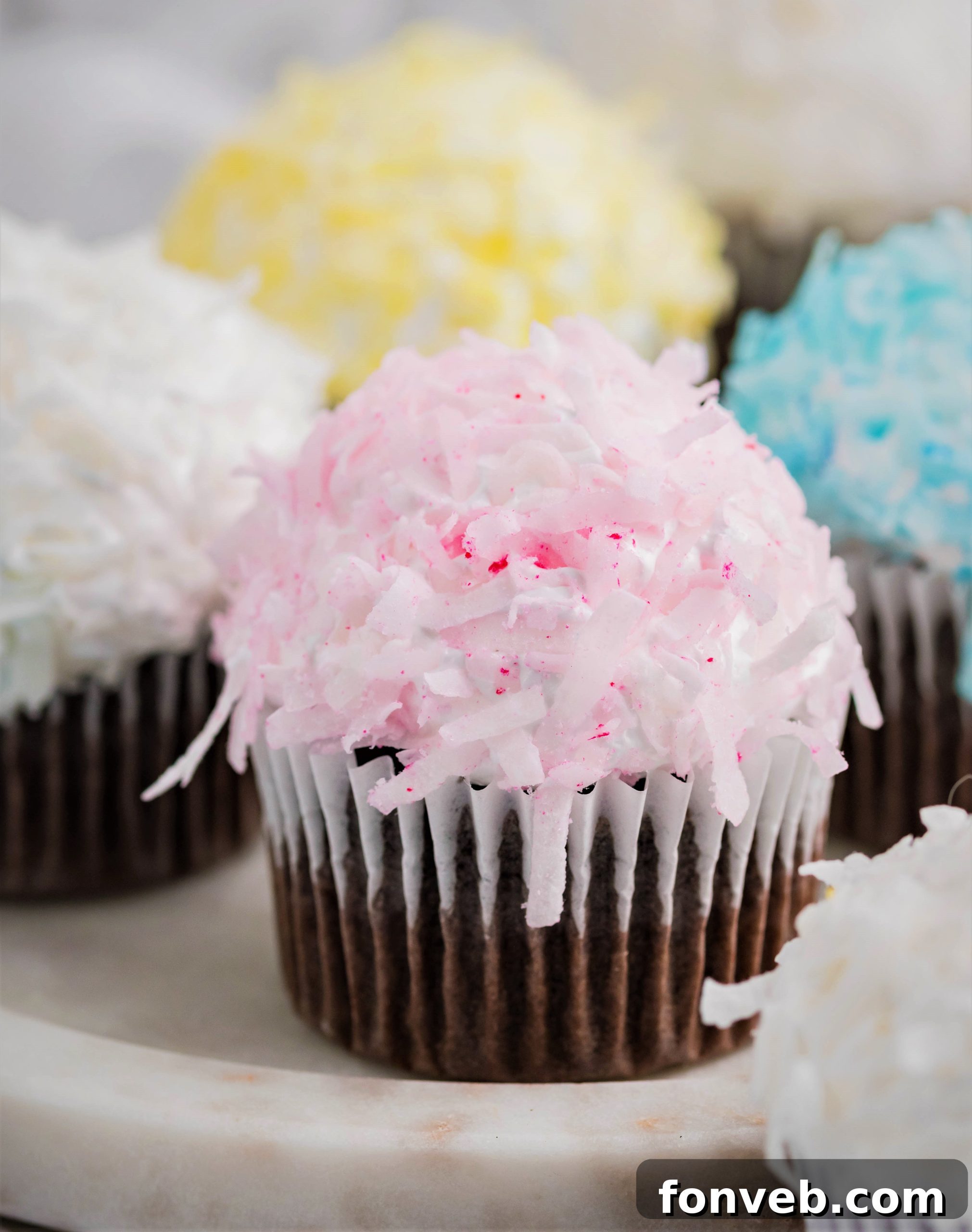 Assortment of pink, yellow, white, and blue chocolate cupcakes topped with coconut
