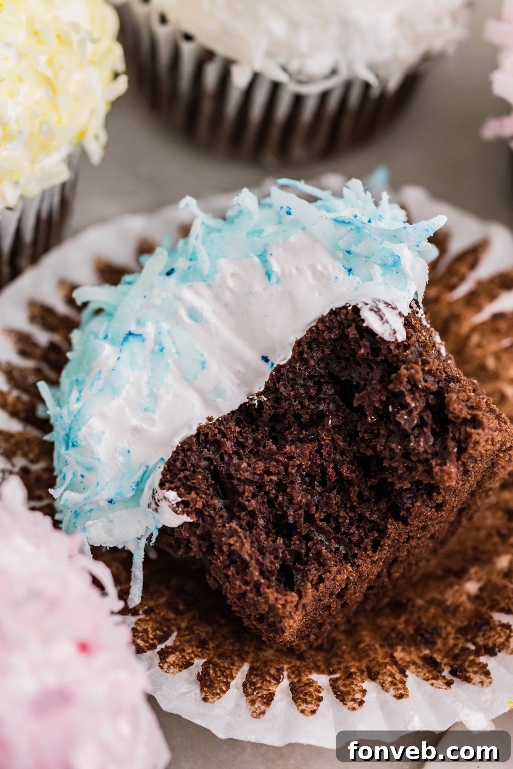 Chocolate cupcake with blue coconut shavings, marshmallow frosting laying down on its side with a bite taken out of it