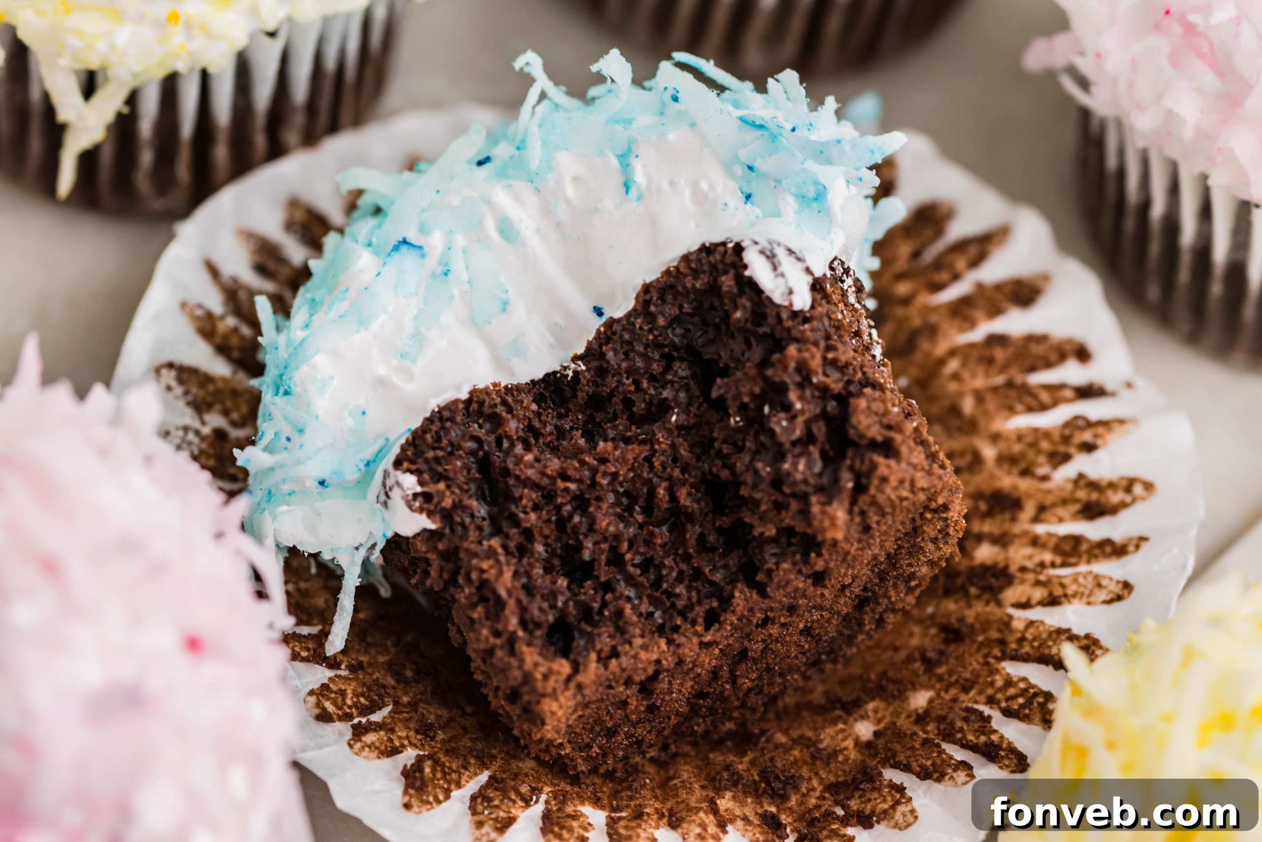 Chocolate cupcake with blue coconut shavings, marshmallow frosting laying down on its side with a bite taken out of it