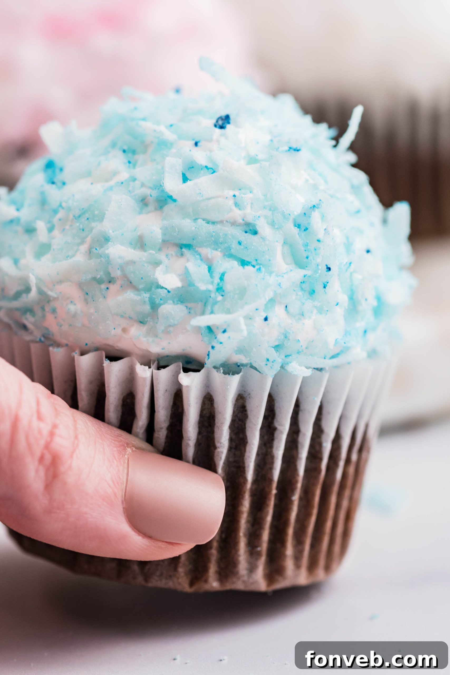 Chocolate cupcake with blue coconut shavings & marshmallow frosting being picked up