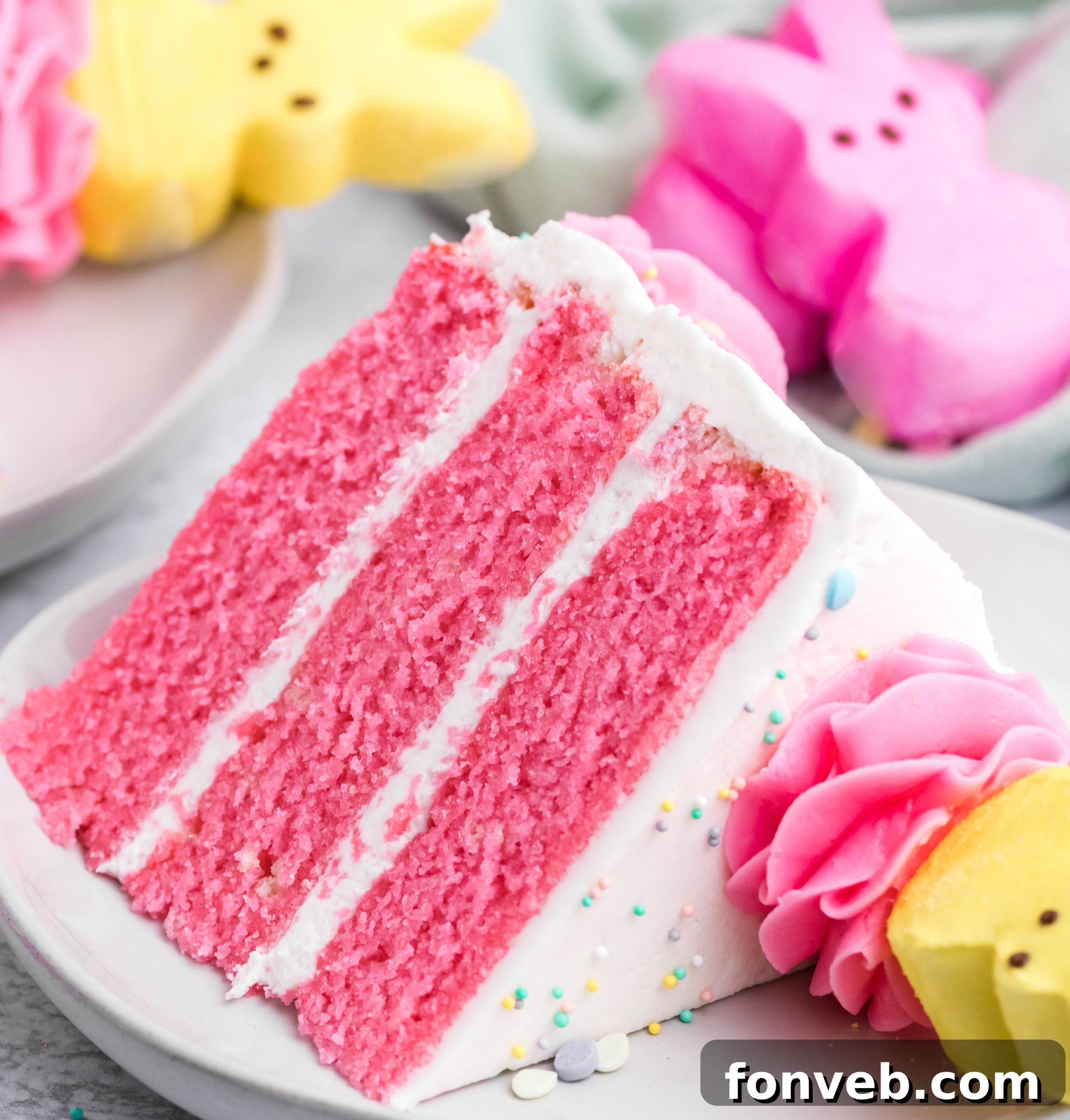 Pink Vanilla layered cake with white frosting and topped with yellow peeps for easter on a white plate with a bit gone