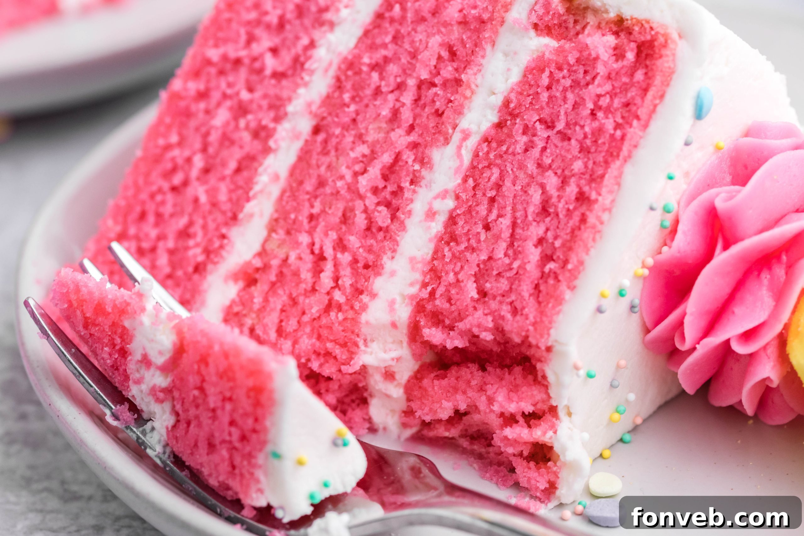 Pink Vanilla layered cake with white frosting and topped with yellow peeps for easter on a white plate with a bit gone and a bite on a fork ready to be eaten