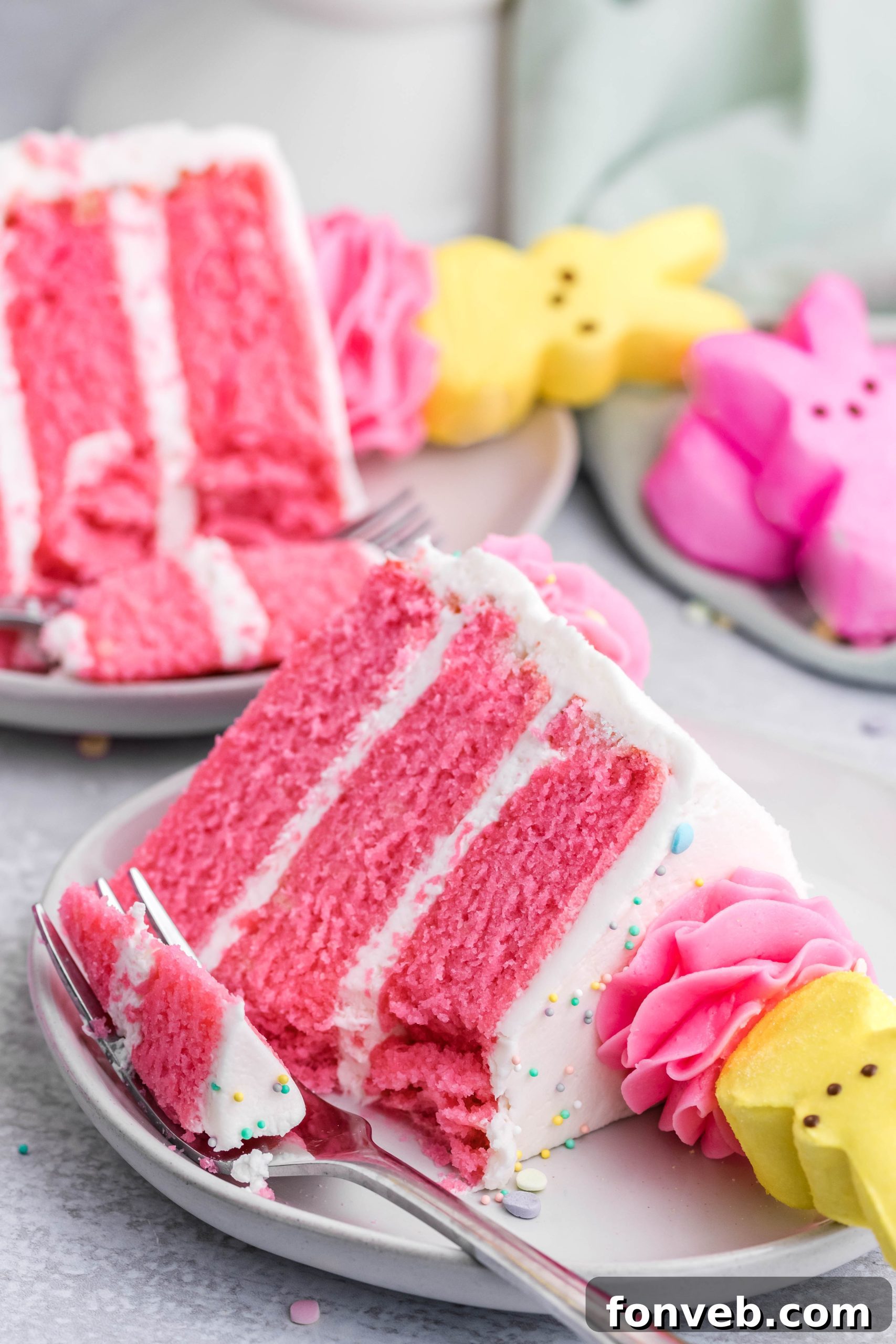 Pink Vanilla layered cake with white frosting and topped with yellow peeps for easter on a white plate with a bit gone