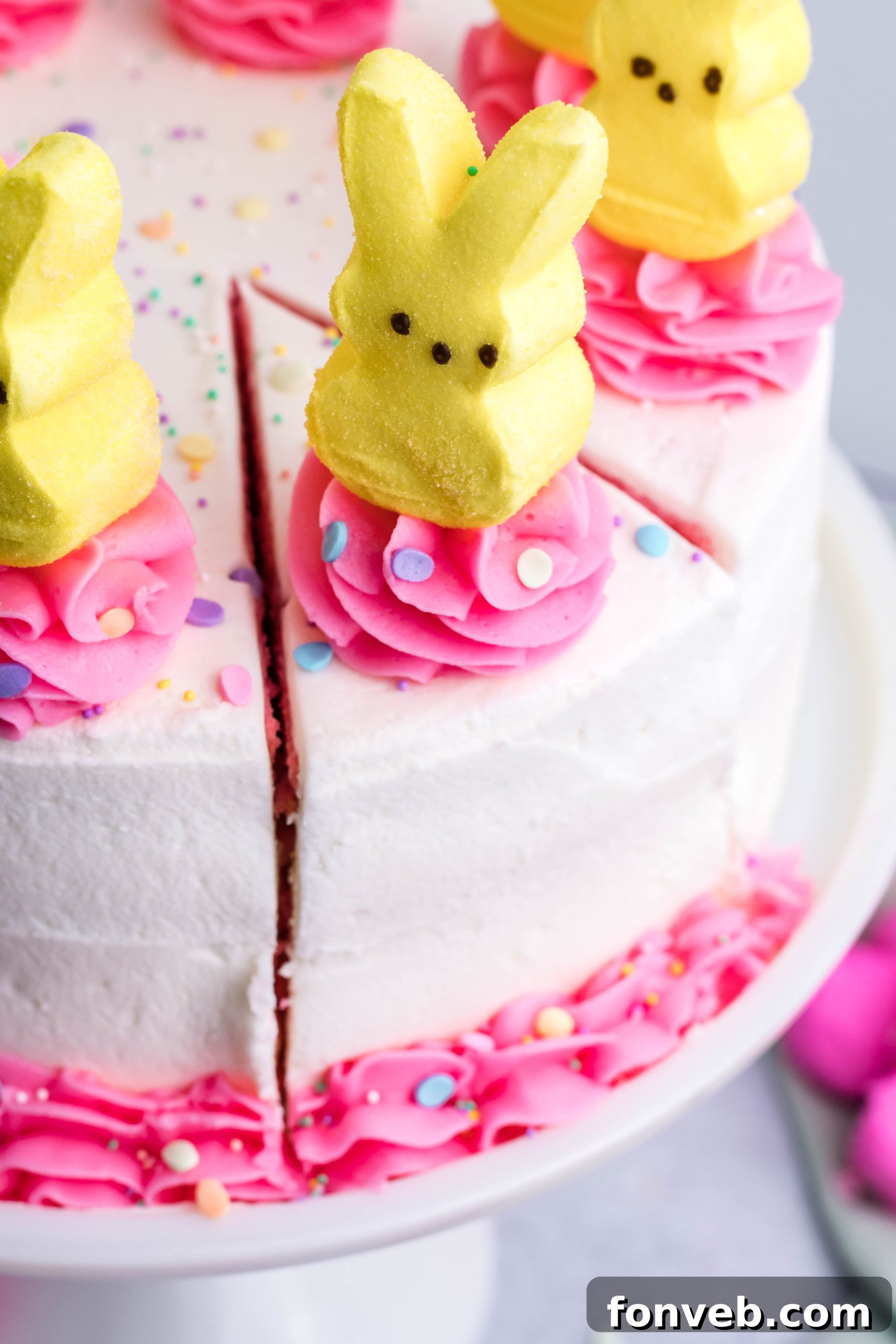 Pink Vanilla layered cake with white frosting and topped with yellow peeps for easter on a white cake stand overhead shot