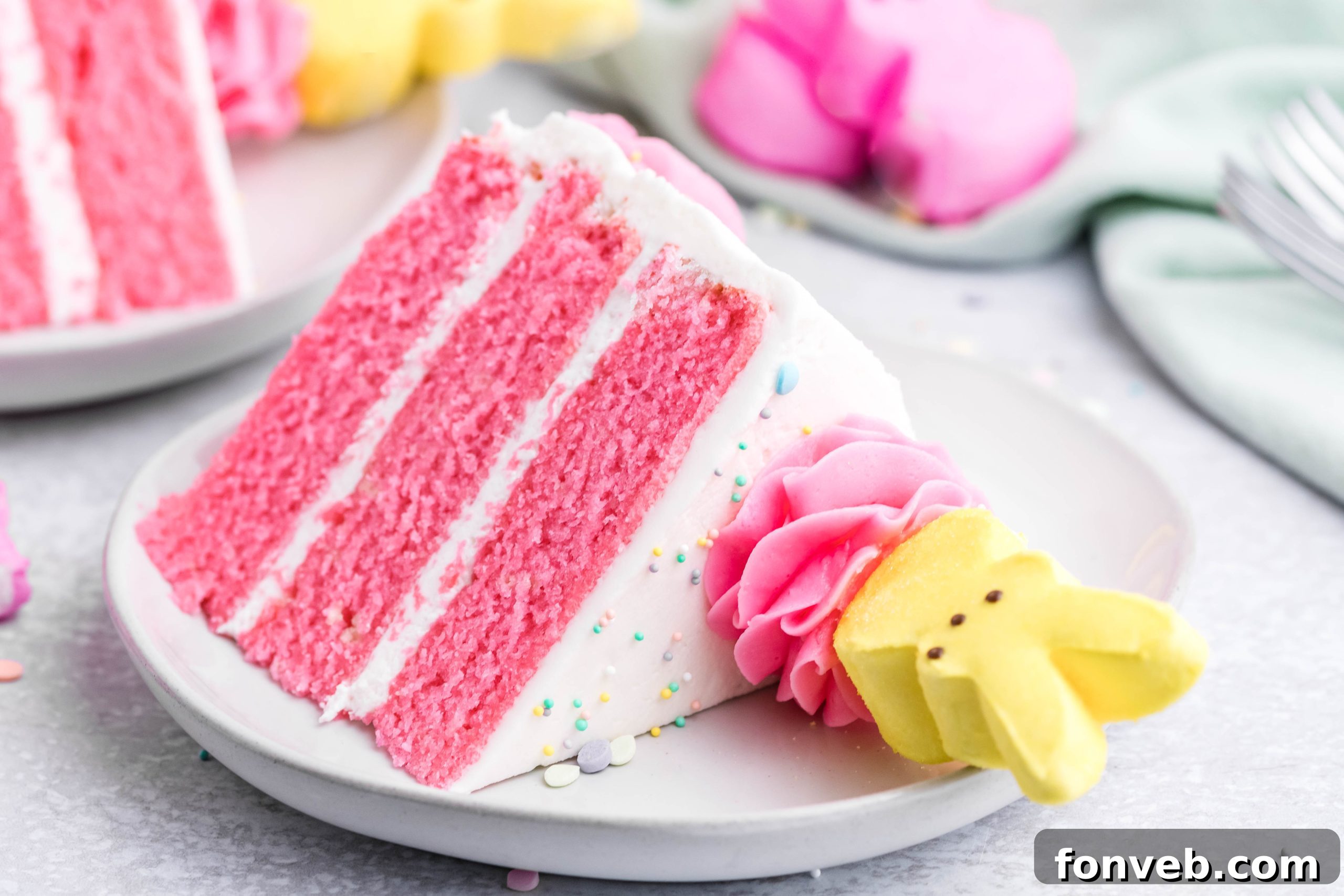Pink Vanilla layered cake with white frosting and topped with yellow peeps for easter on a white plate 