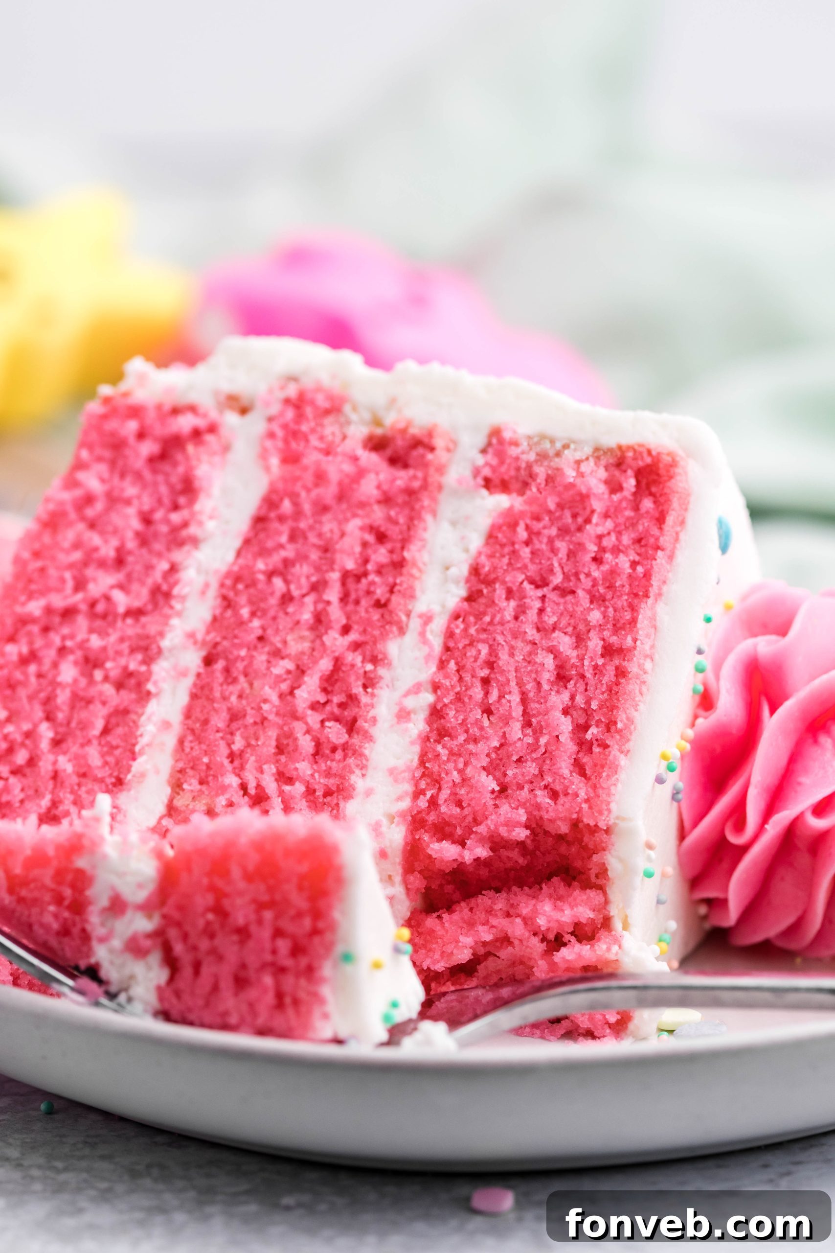 Pink Vanilla layered cake with white frosting and topped with yellow peeps for easter on a white plate with a bit gone