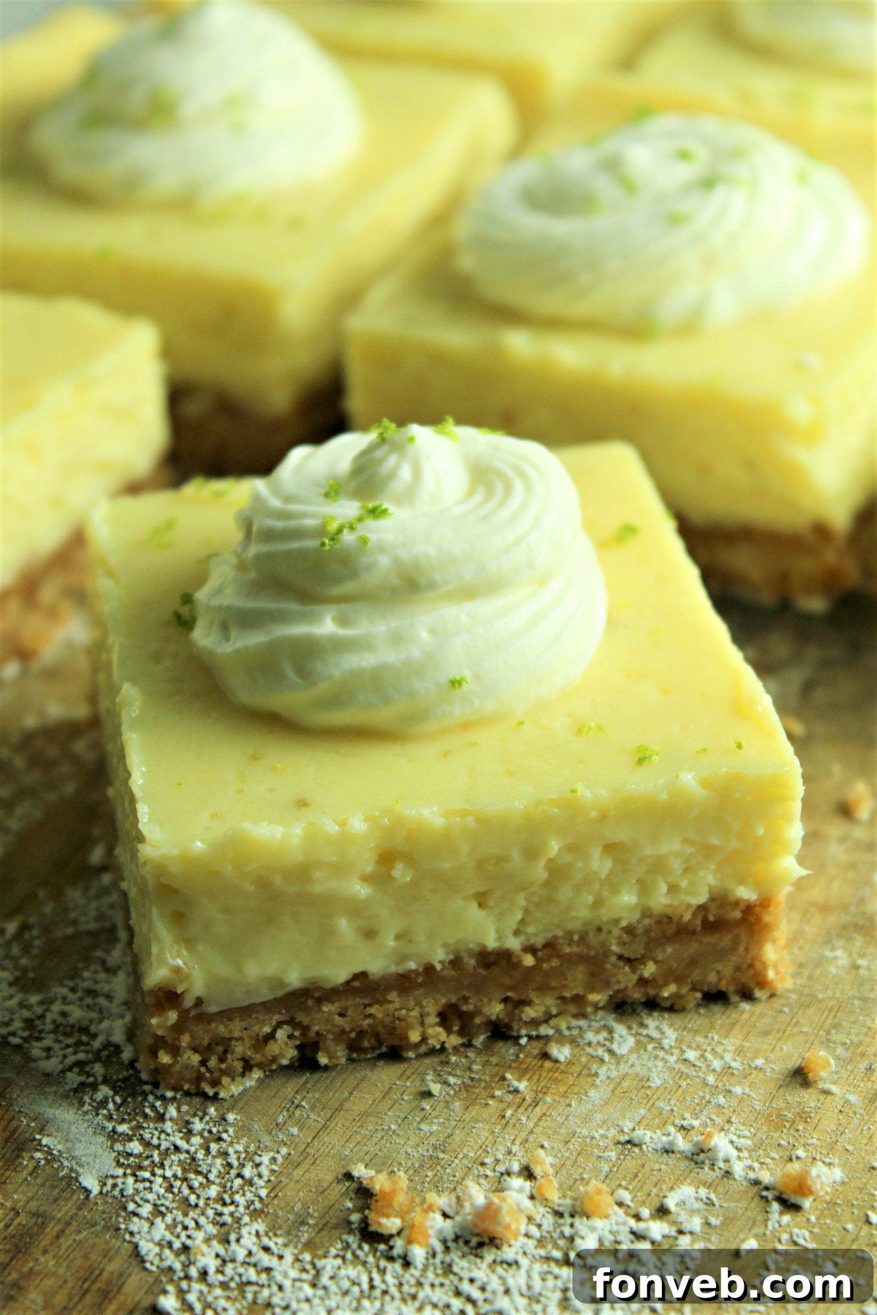 Key Lime Bars with lime whipped cream topped with lime zest on counter with crumbs around