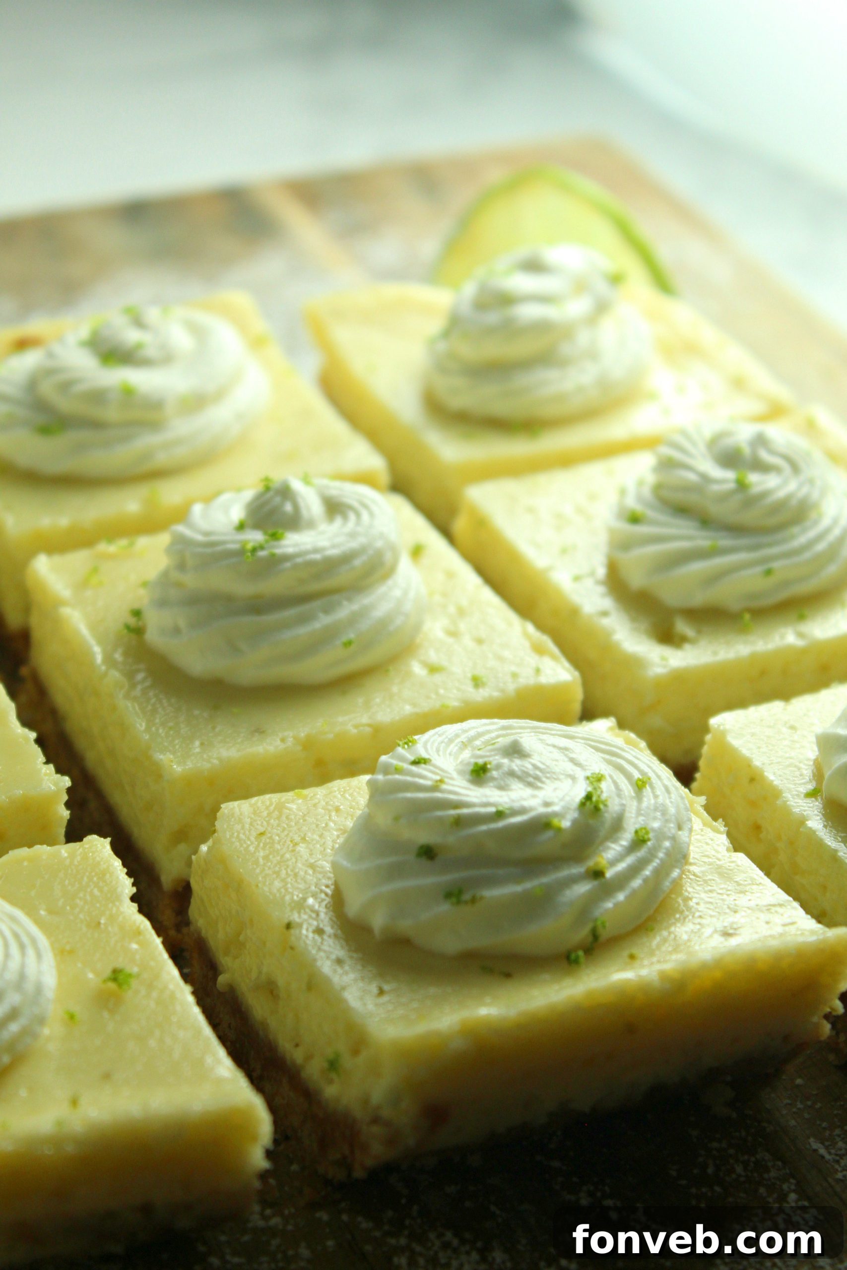 Key Lime Bars with lime whipped cream topped with lime zest on a baking sheet from the side
