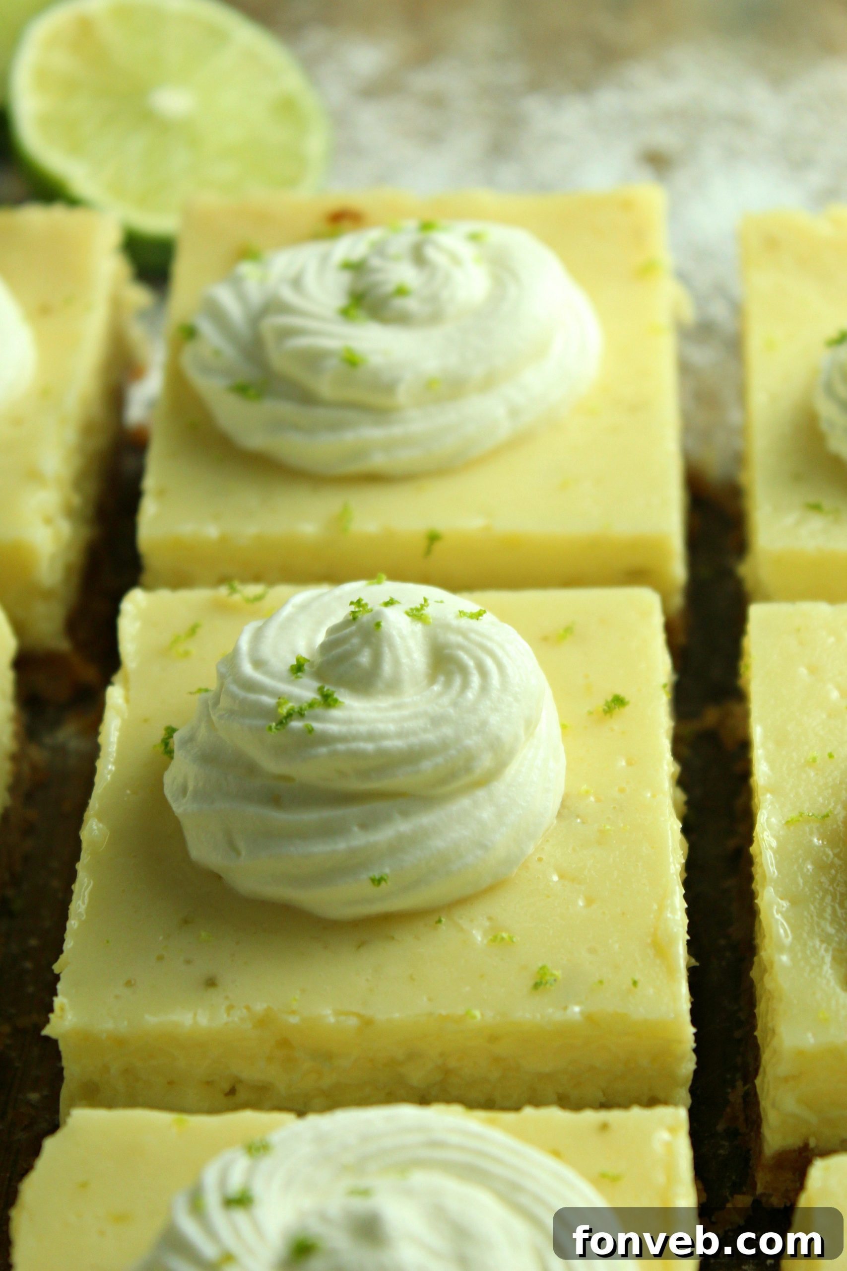 Key Lime Bars with lime whipped cream topped with lime zest on a baking sheet