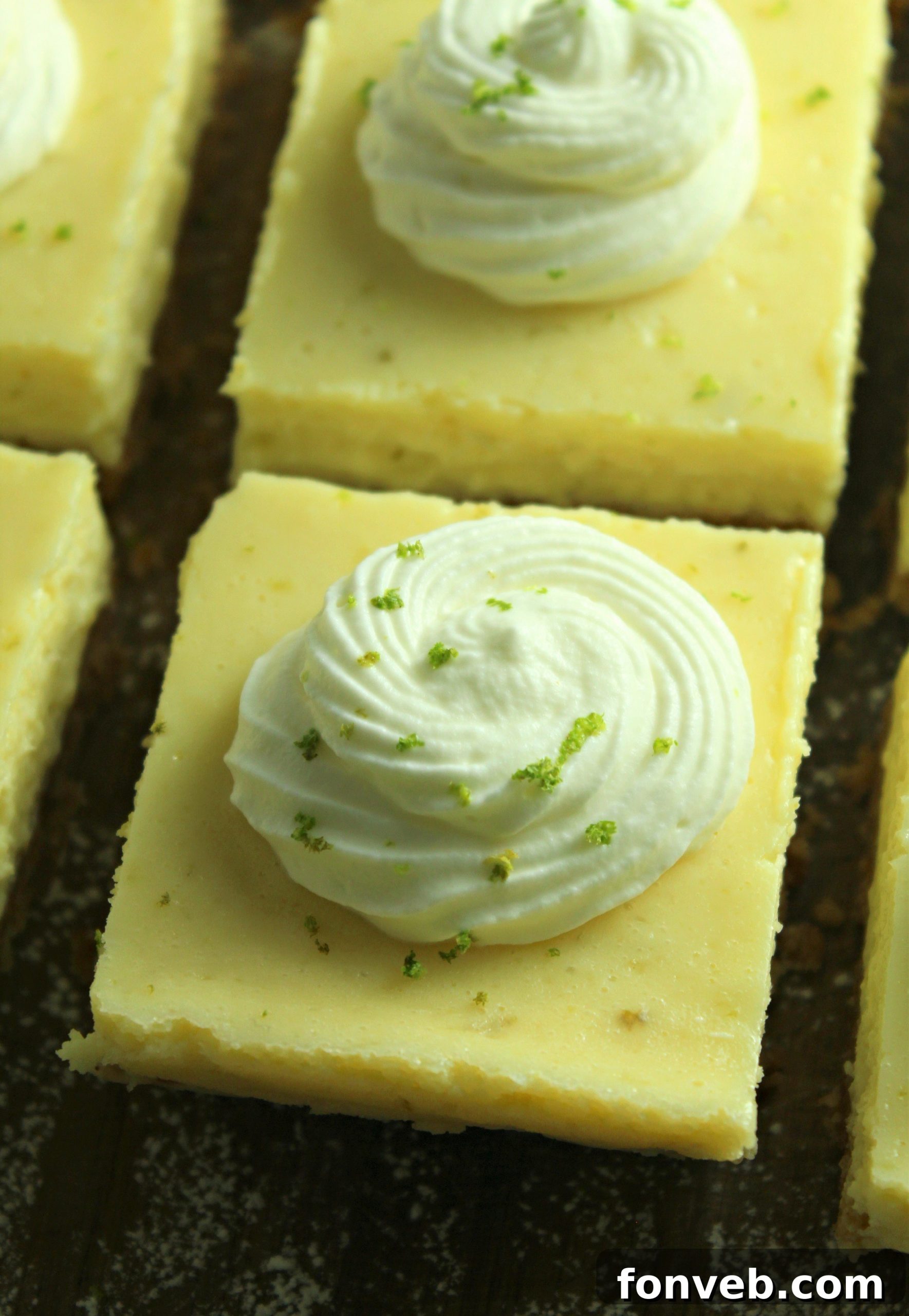 Key Lime Bars with lime whipped cream topped with lime zest on a baking sheet