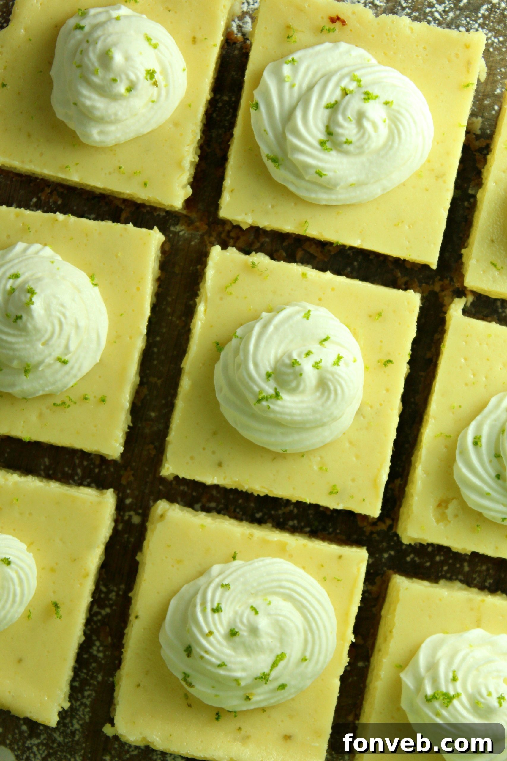Key Lime Bars with lime whipped cream topped with lime zest on a baking sheet overhead