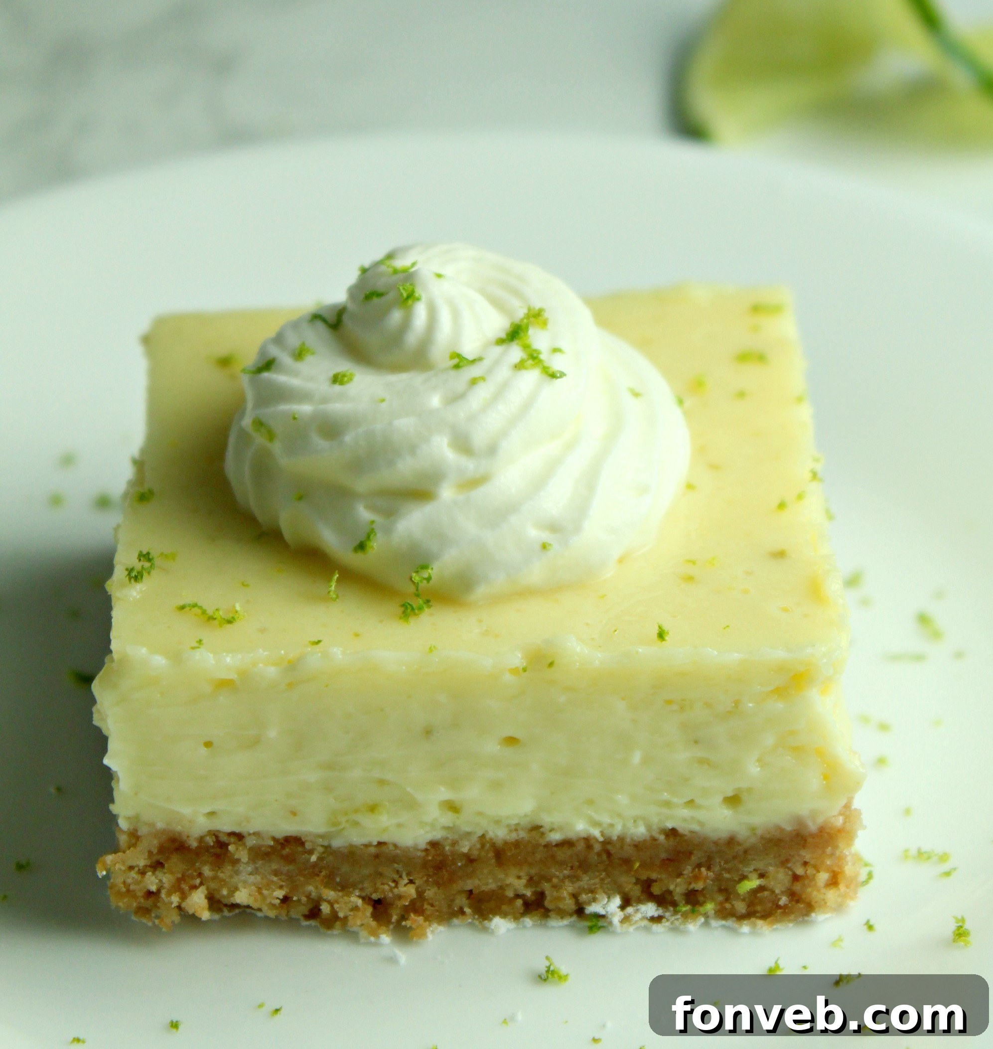 Key Lime Bars with lime whipped cream topped with lime zest on a white plate