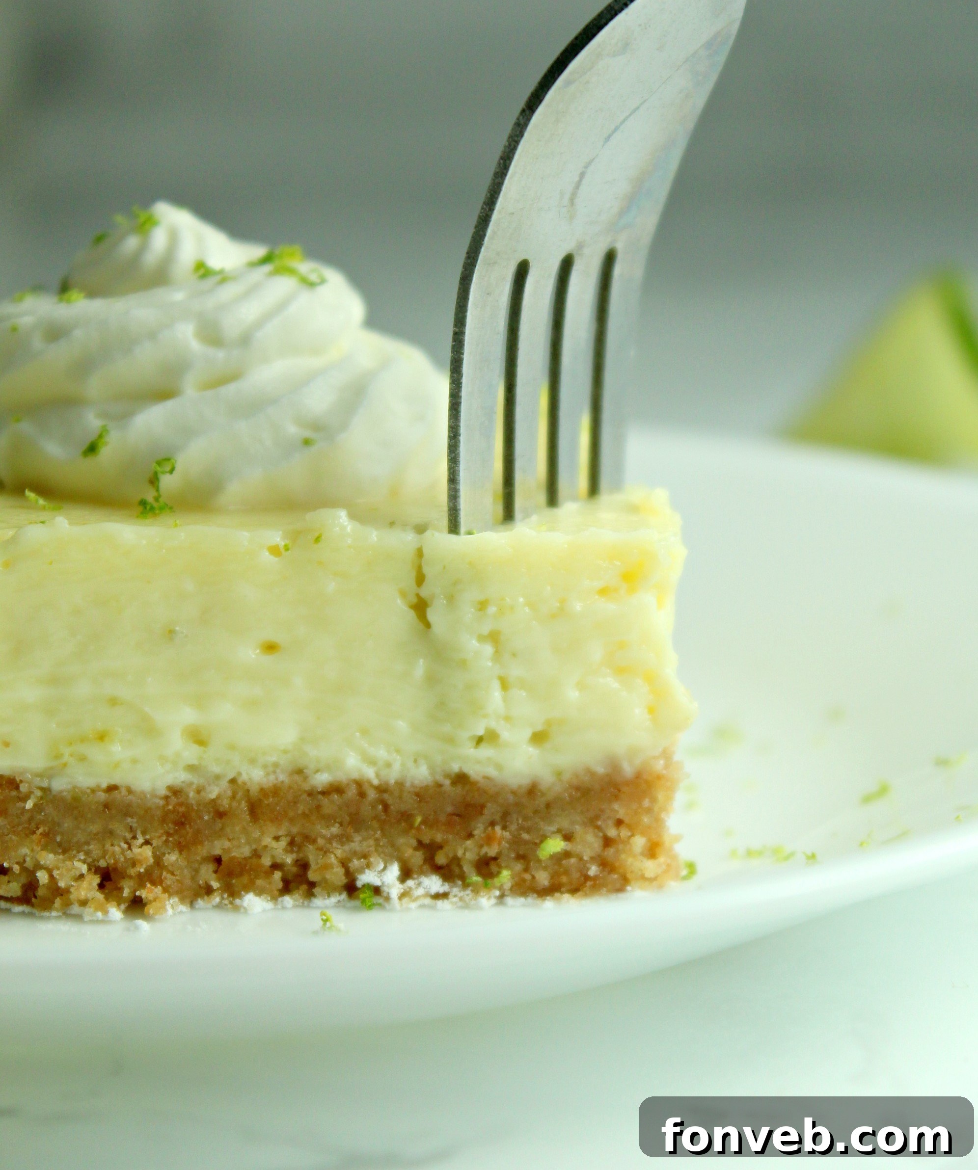 Key Lime Bars with lime whipped cream topped with lime zest on a white plate with a fork cutting into it