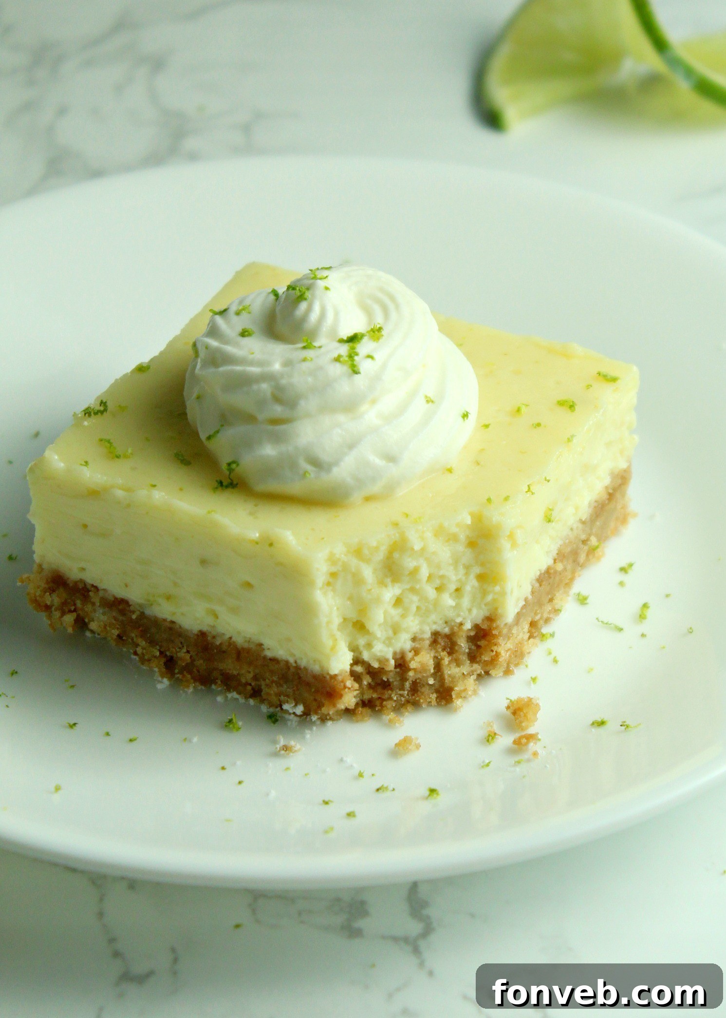 Key Lime Bars with lime whipped cream topped with lime zest on a white plate with a bite gone