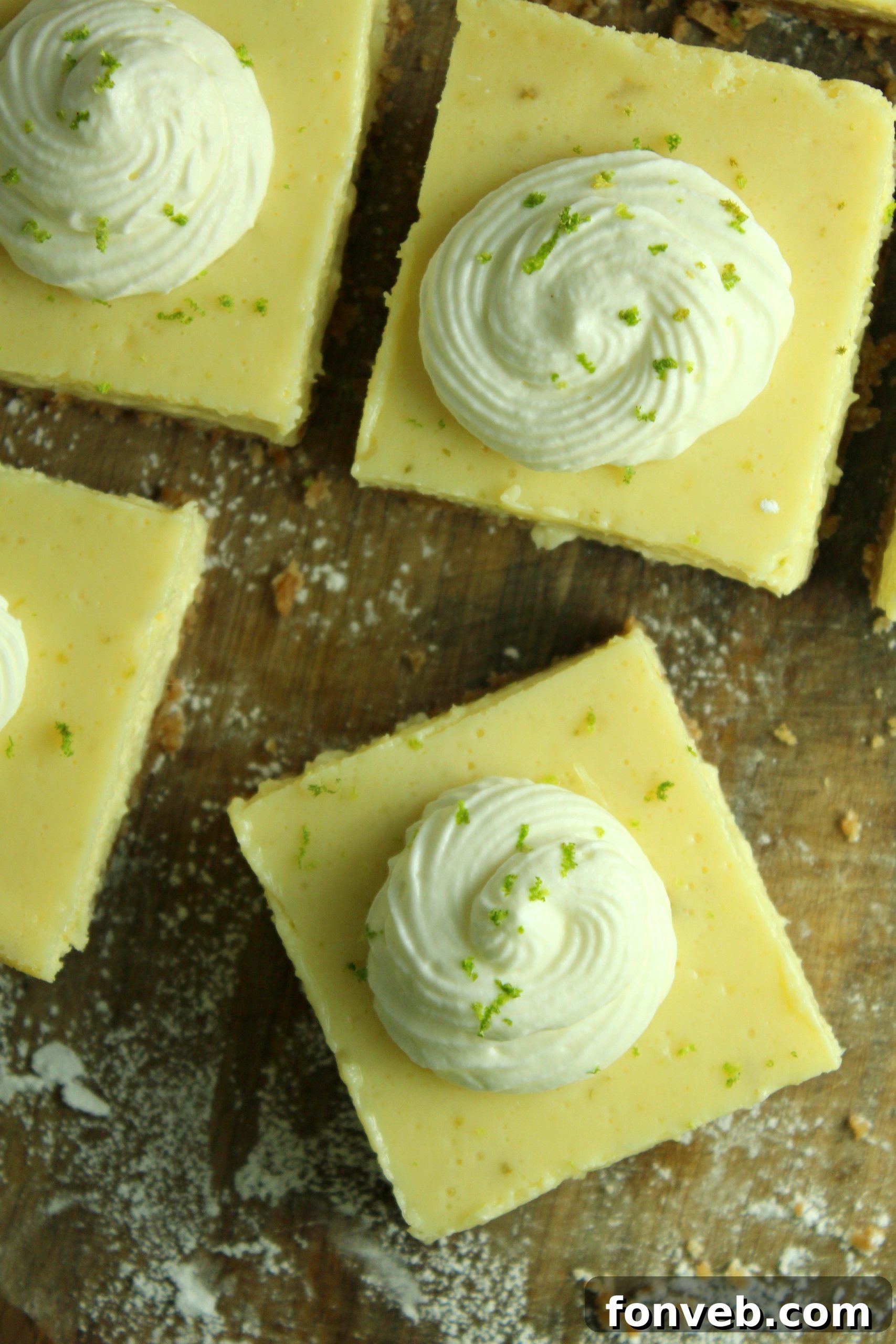 Key Lime Bars with lime whipped cream topped with lime zest on a wood table