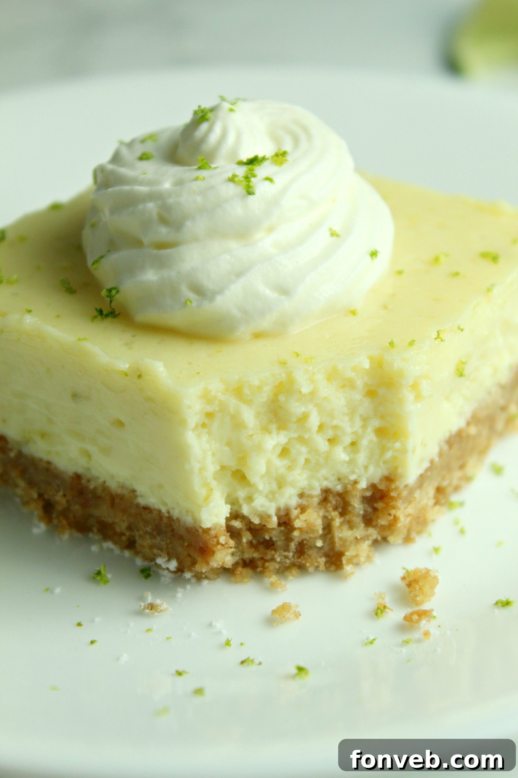 Key Lime Bars with lime whipped cream topped with lime zest on a white plate with a bite taken out