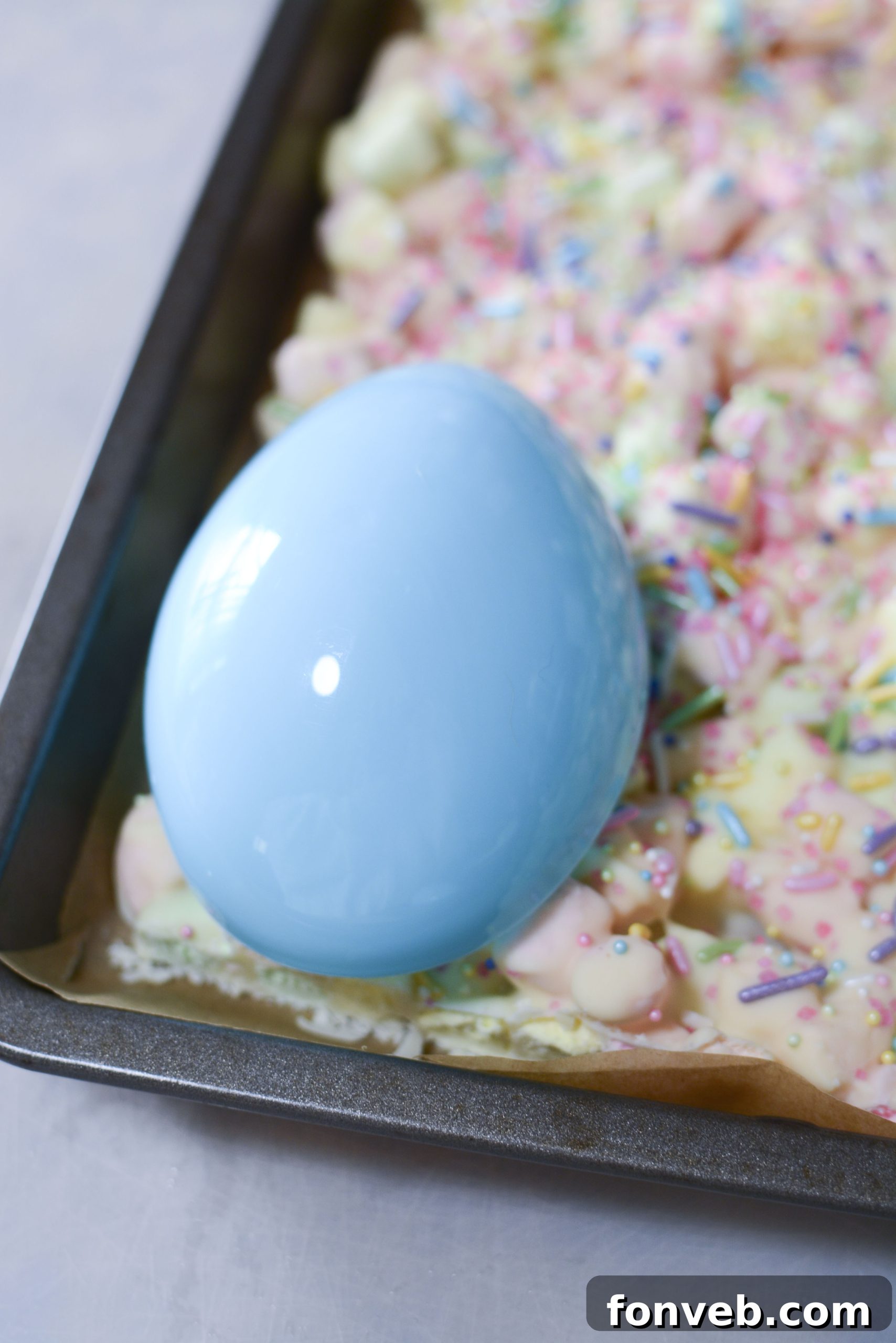 Easter Marshmallow treats with pink, green and yellow mini marshmallows on a cookie sheet with a plastic egg cutting out a treat