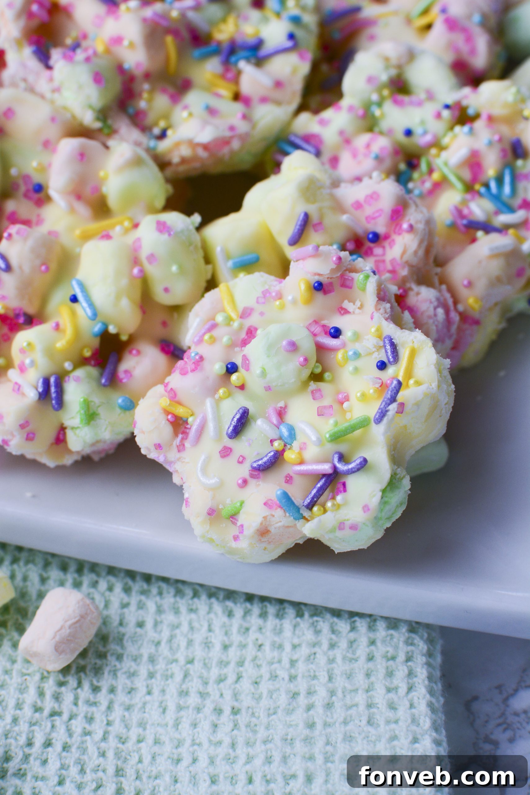 Easter Marshmallow treats with pink, green and yellow mini marshmallows cut into the shape of flowers on a square white plate