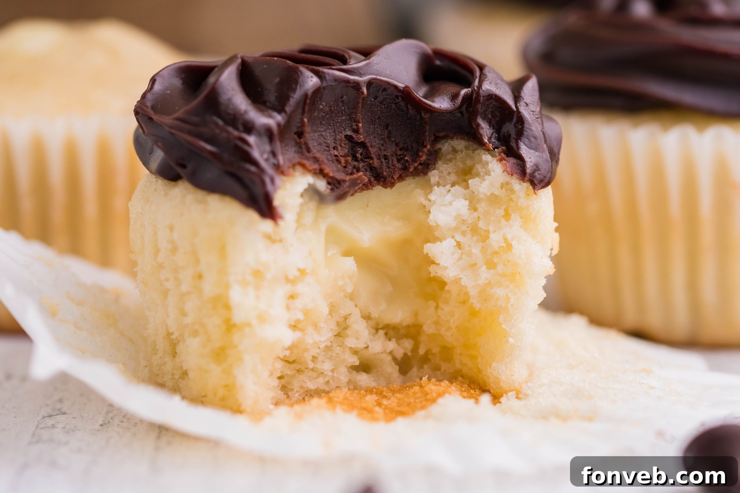side shot of Boston Cream Cupcakes on a white counter with a bite gone