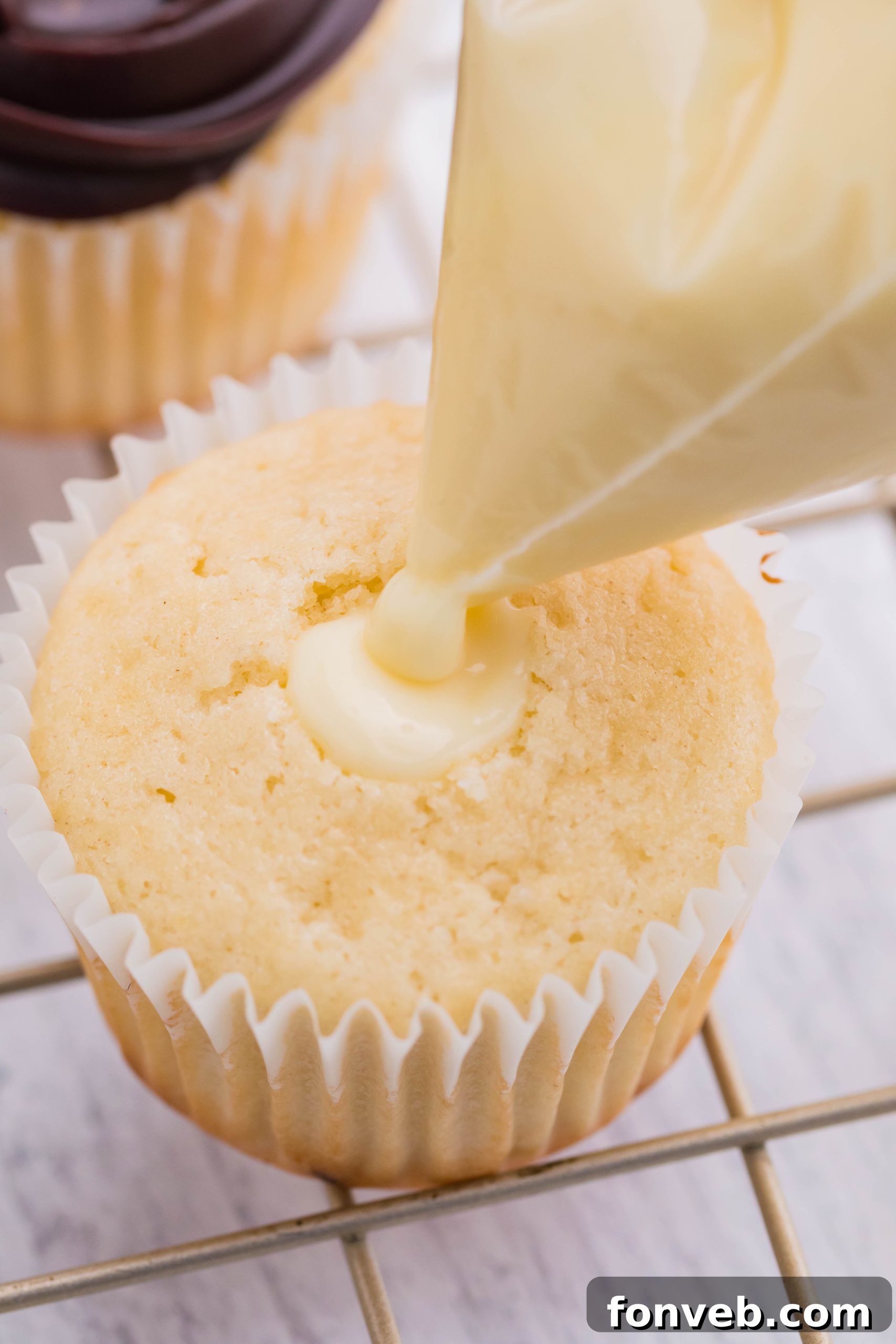 Piping the cream filling into the center of the boston cream cupcake