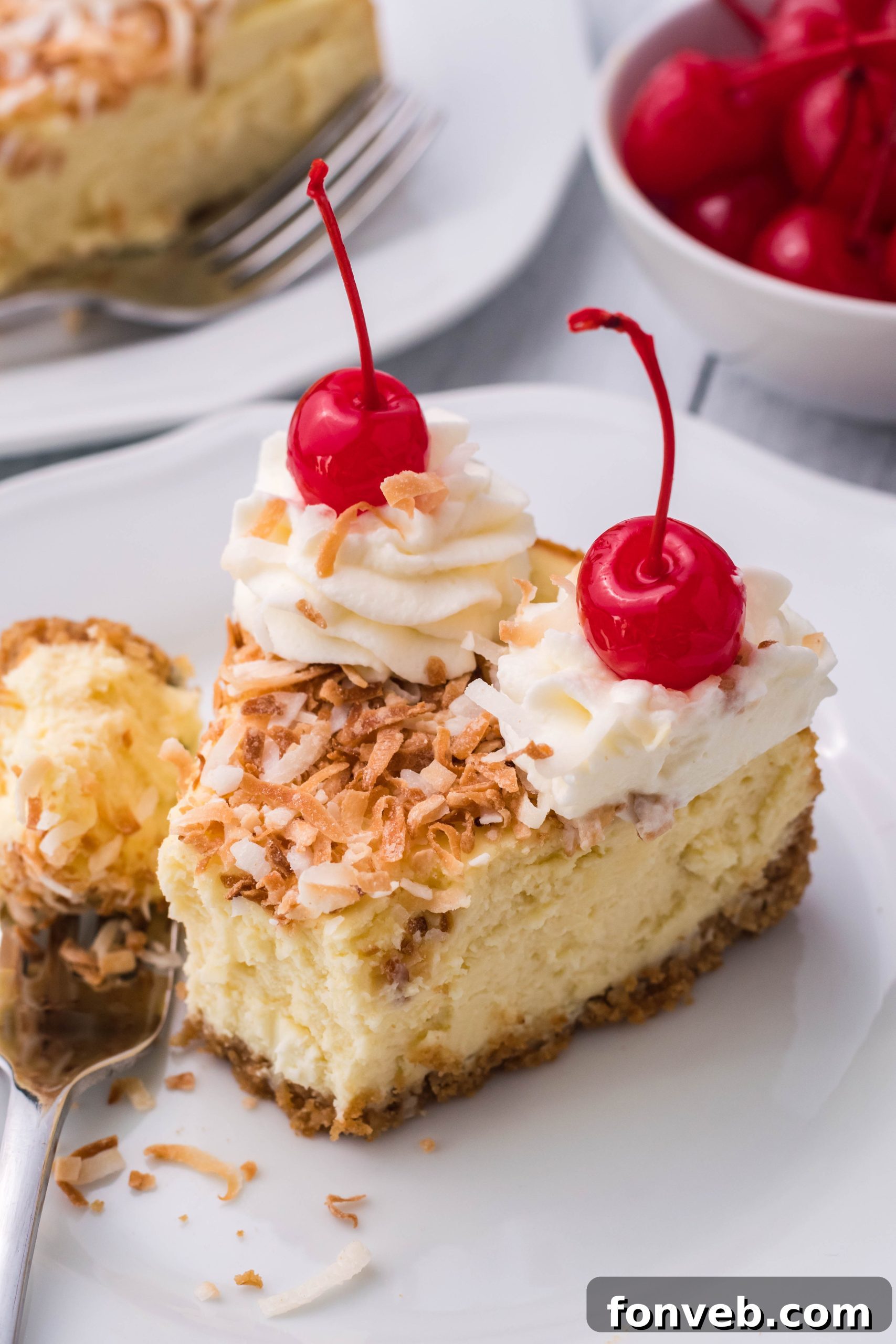 Delicious Coconut Cheesecake on a white plate topped with vibrant cherries and fluffy whipped cream, captured from an overhead angle.