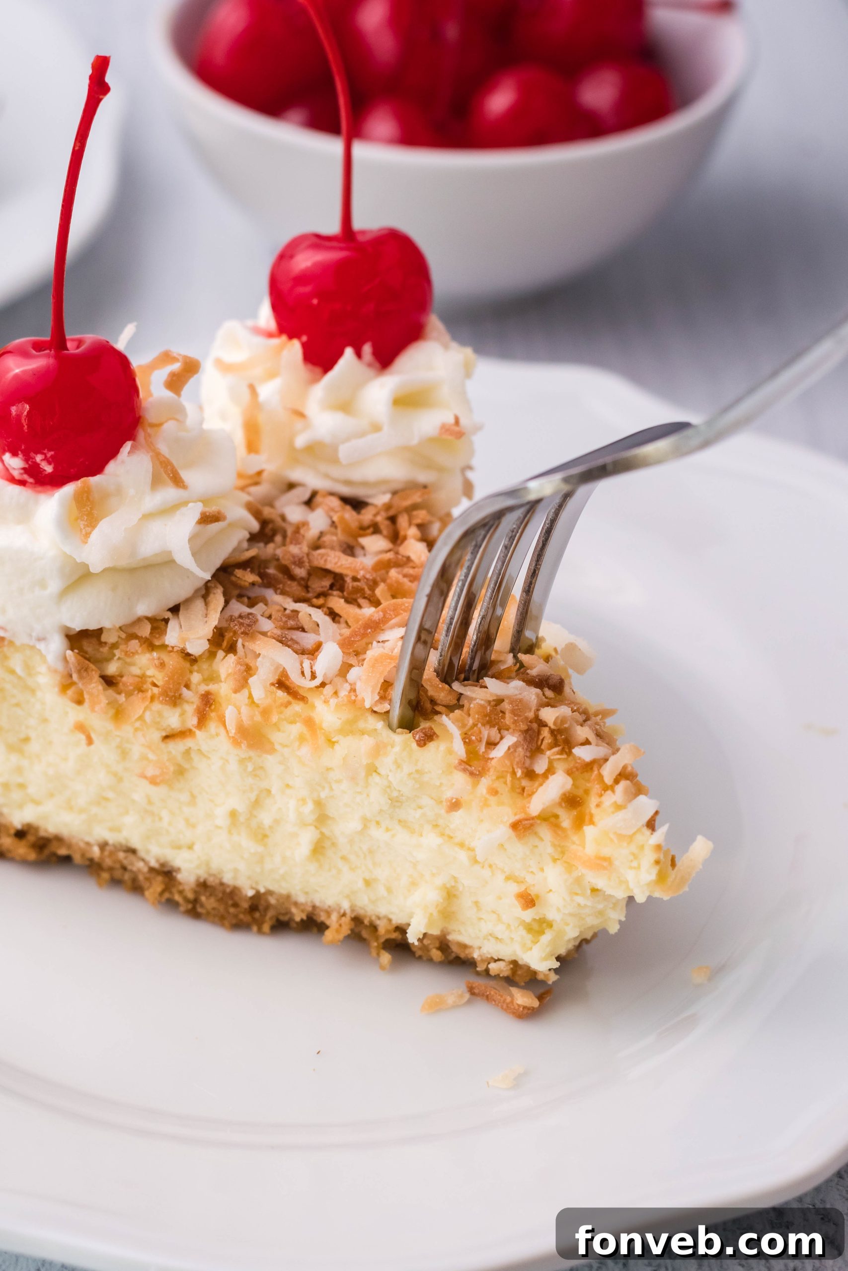A fork gently slices into a generous piece of Coconut Cheesecake, revealing its creamy interior and luscious toppings.