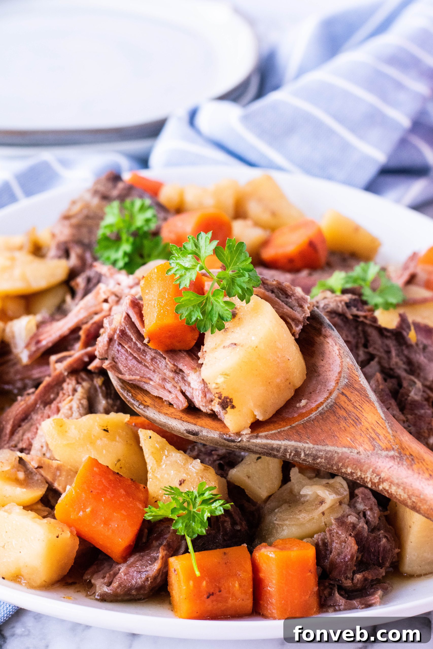 crock pot chuck roast on a plate with potatoes and carrots being lifted with a spoon