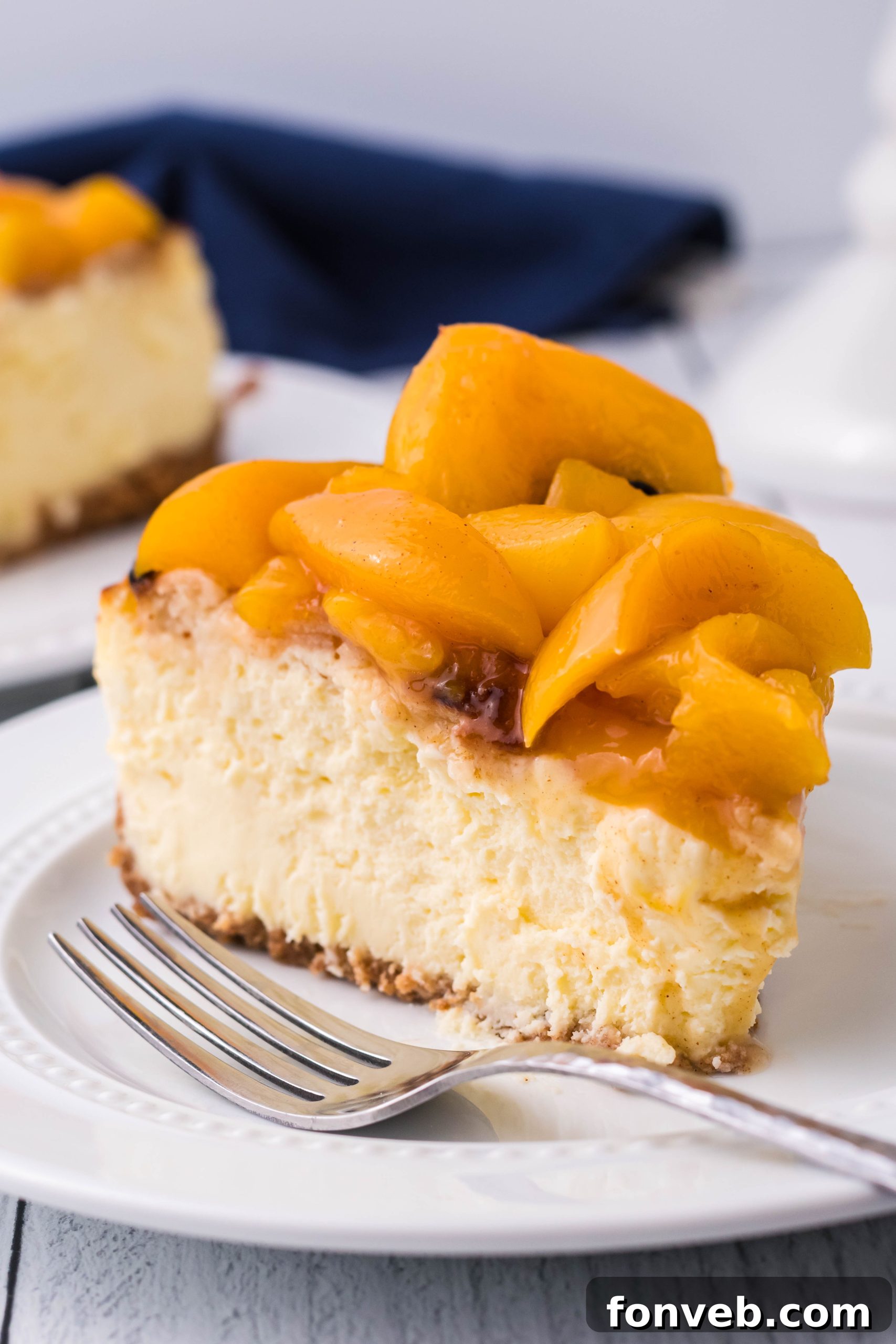 Peach Cobbler Cheesecake on a white plate, viewed from a slight side angle, showcasing its height and layers.
