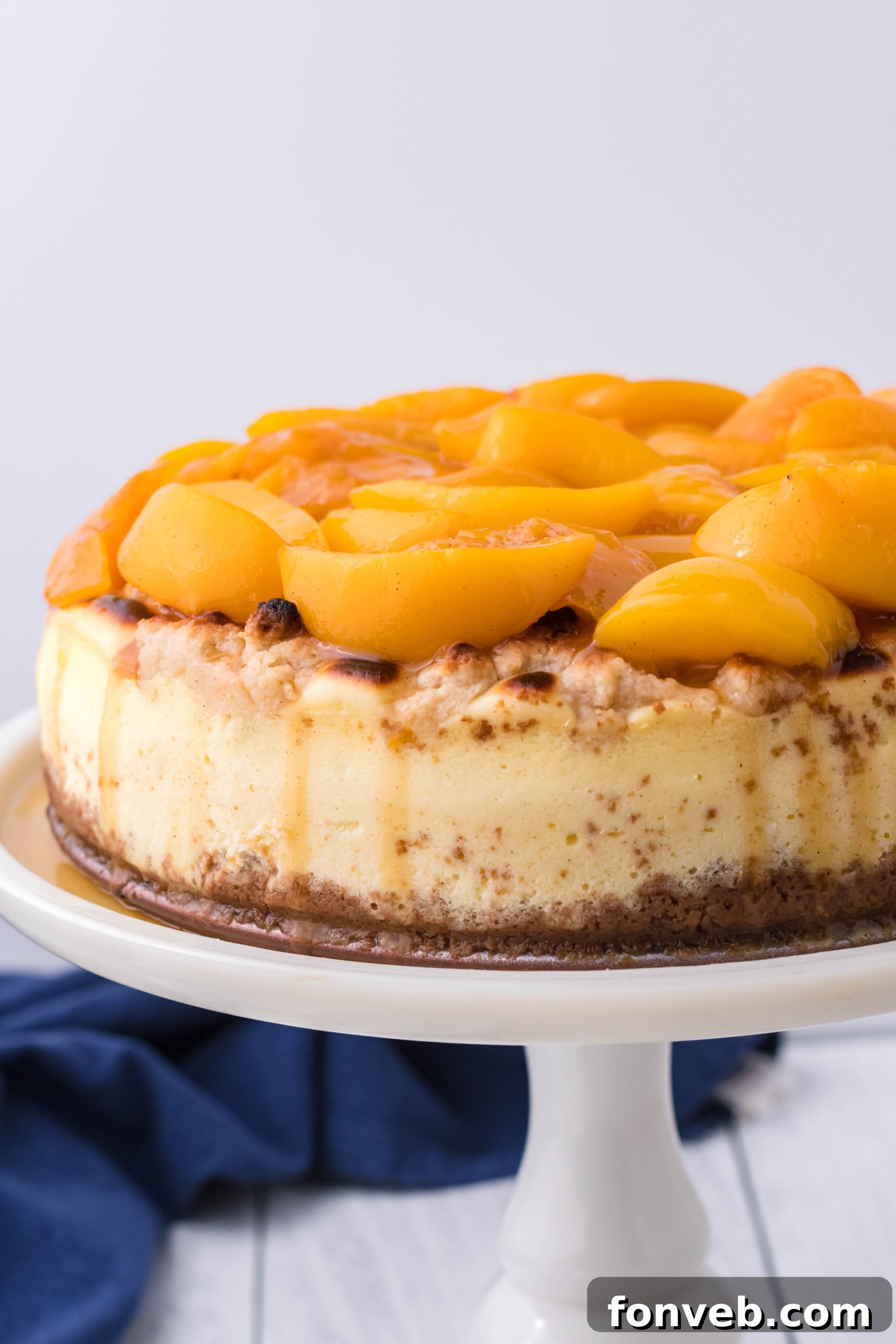 A whole Peach Cobbler Cheesecake elegantly displayed on a white cake stand.