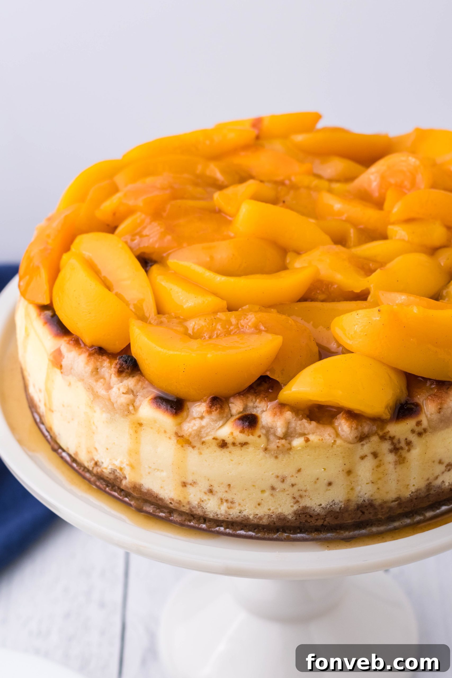 An overhead shot of Peach Cobbler Cheesecake on a white cake stand, showcasing the vibrant peach topping and golden cobbler crumbs.