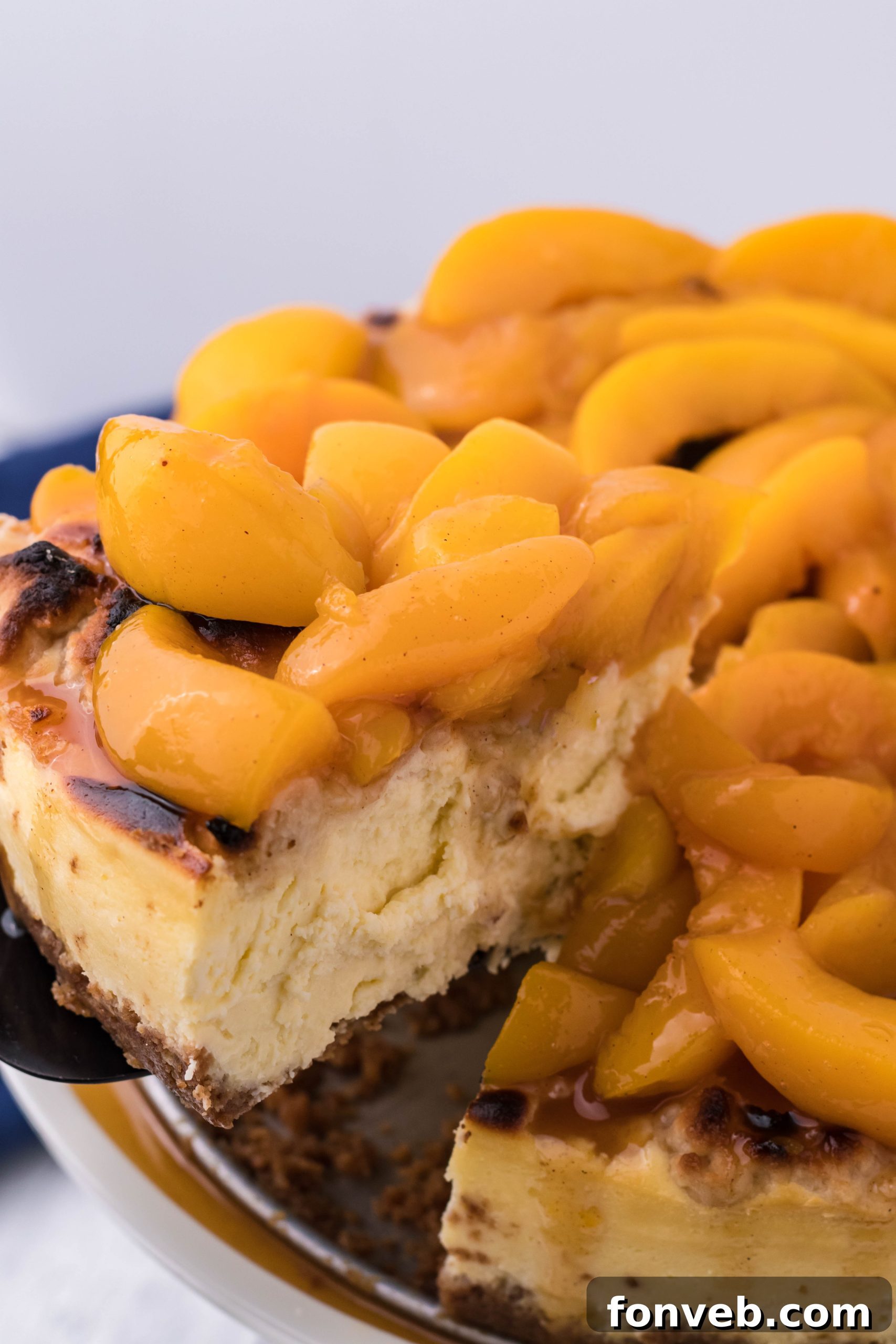 A slice of Peach Cobbler Cheesecake being lifted with a spatula, highlighting its layers.