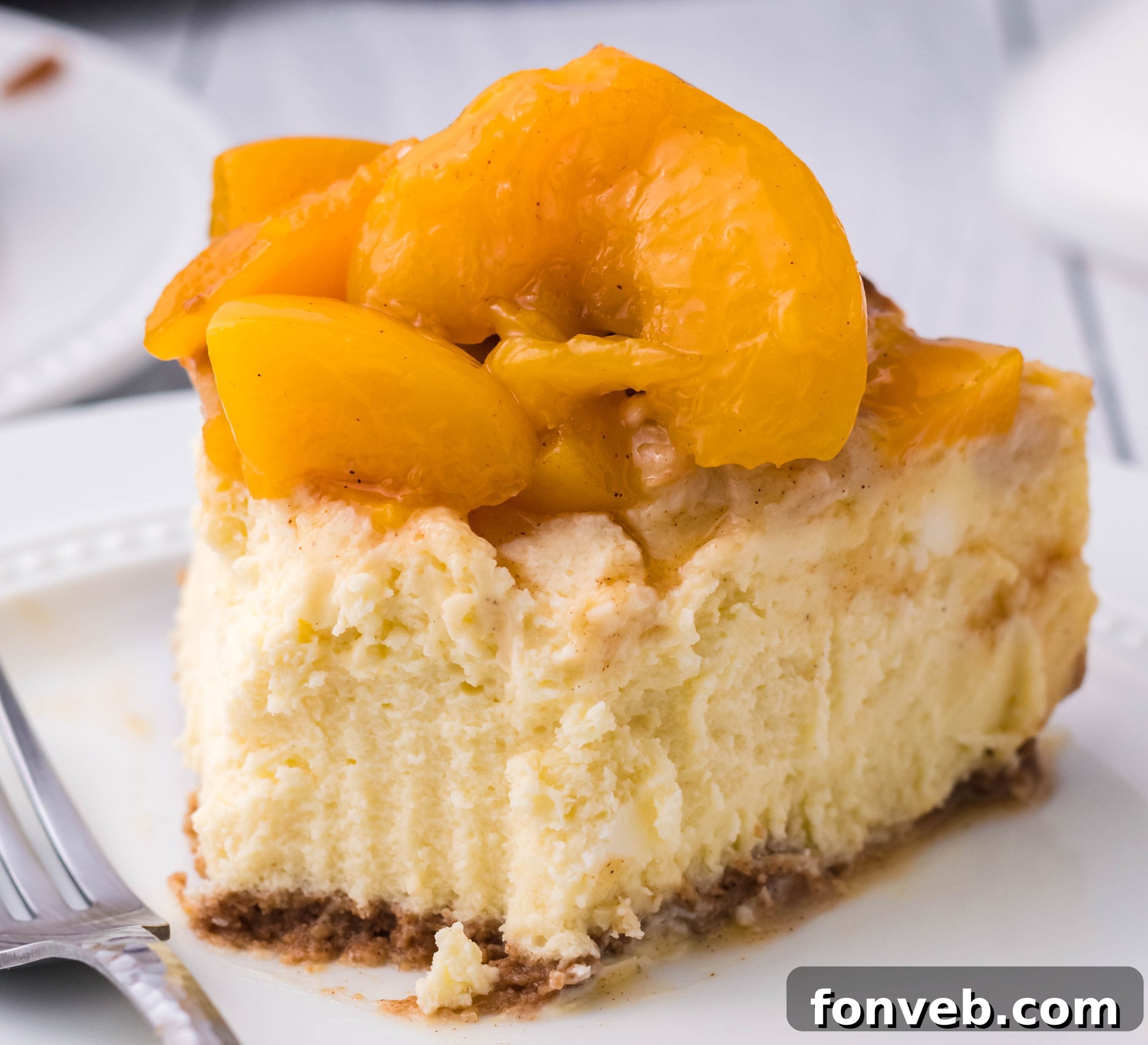 Close-up of a slice of Peach Cobbler Cheesecake on a white plate, showing the golden crust and creamy filling.