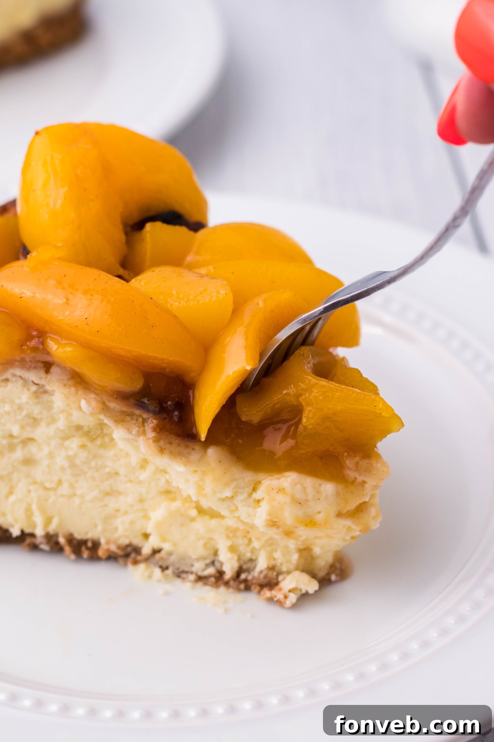 A slice of Peach Cobbler Cheesecake on a white plate, with a fork gently cutting into it.