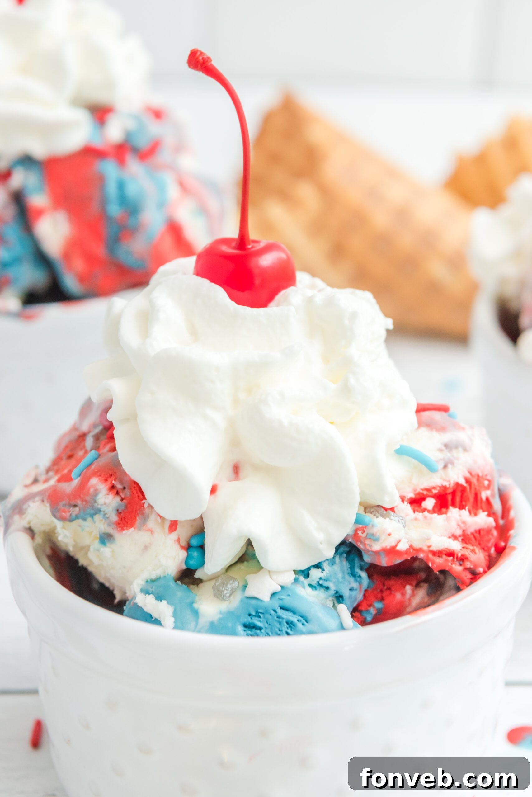 Red, White & Blue Ice Cream in a white bowl topped with whipped cream and a cherry
