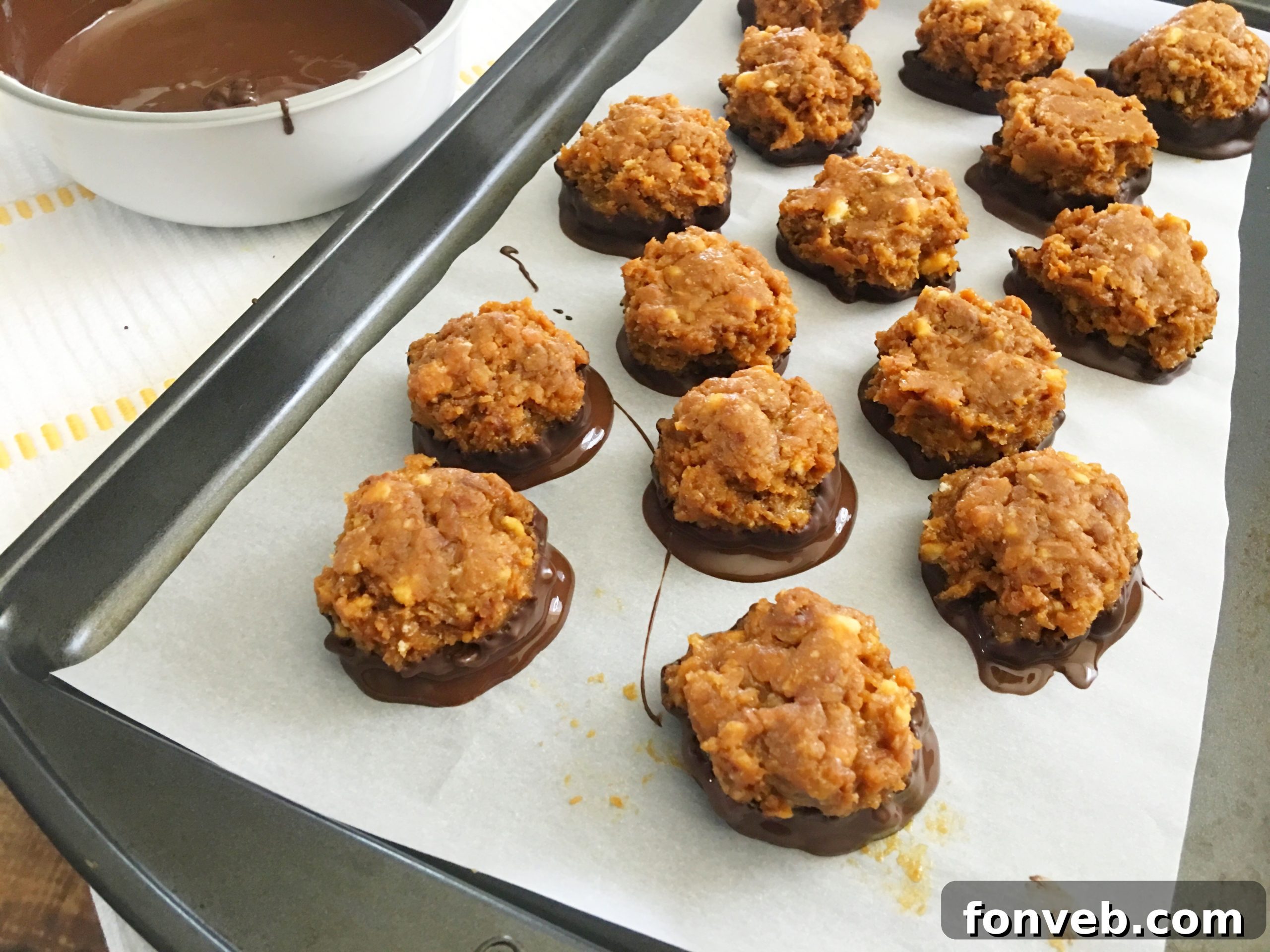 Samoa Bites partially dipped in melted dark chocolate, sitting on a parchment paper-lined baking sheet, waiting for the chocolate to set.