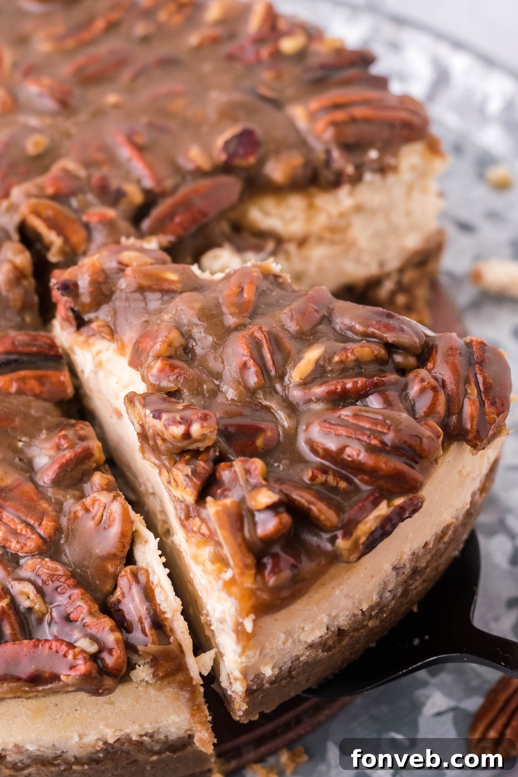 A glorious slice of Pecan Pie Cheesecake being carefully lifted from the whole dessert, showcasing its distinct layers and rich topping.