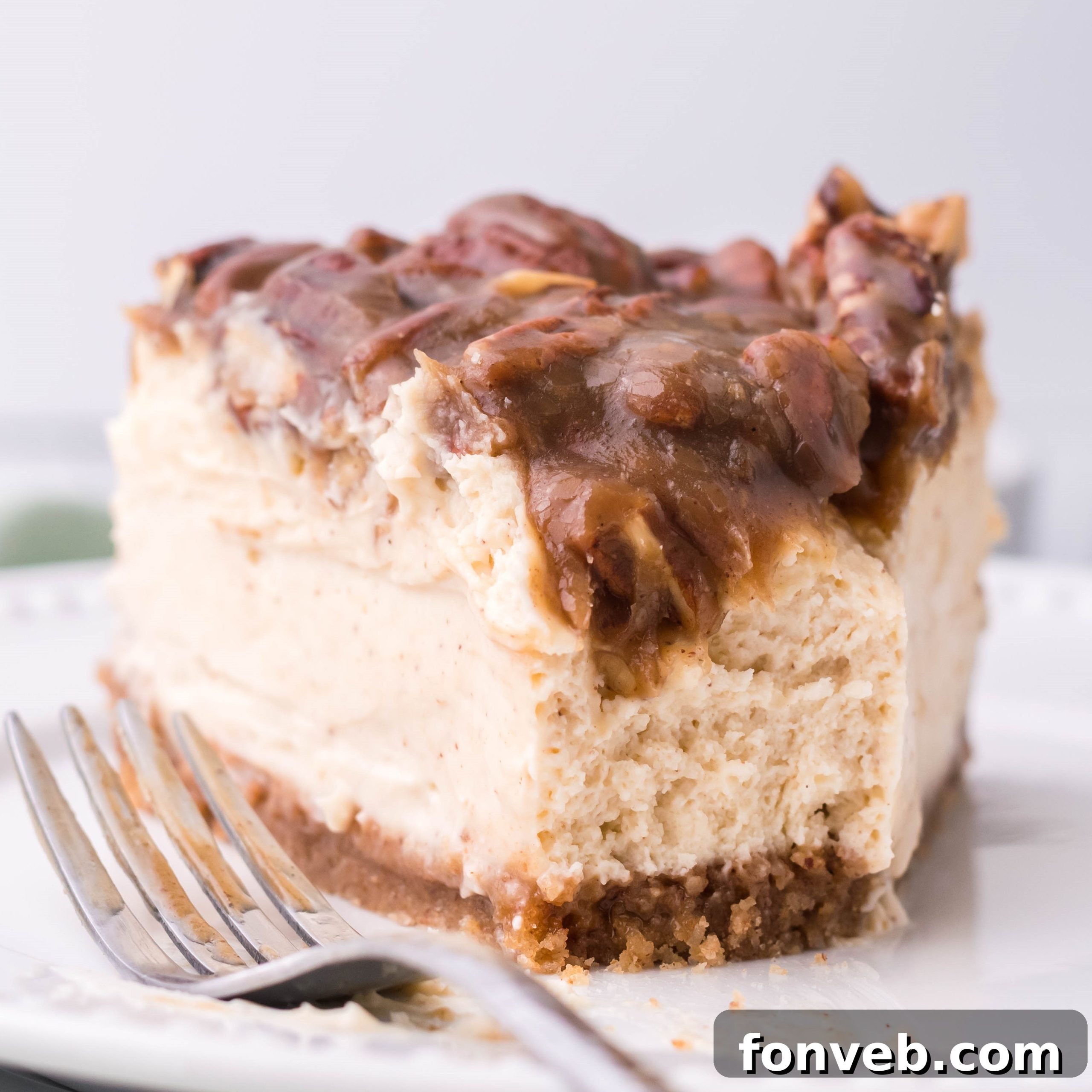 A pristine slice of Pecan Pie Cheesecake on a white plate with a section clearly missing, showcasing its tempting layers after a delightful bite.