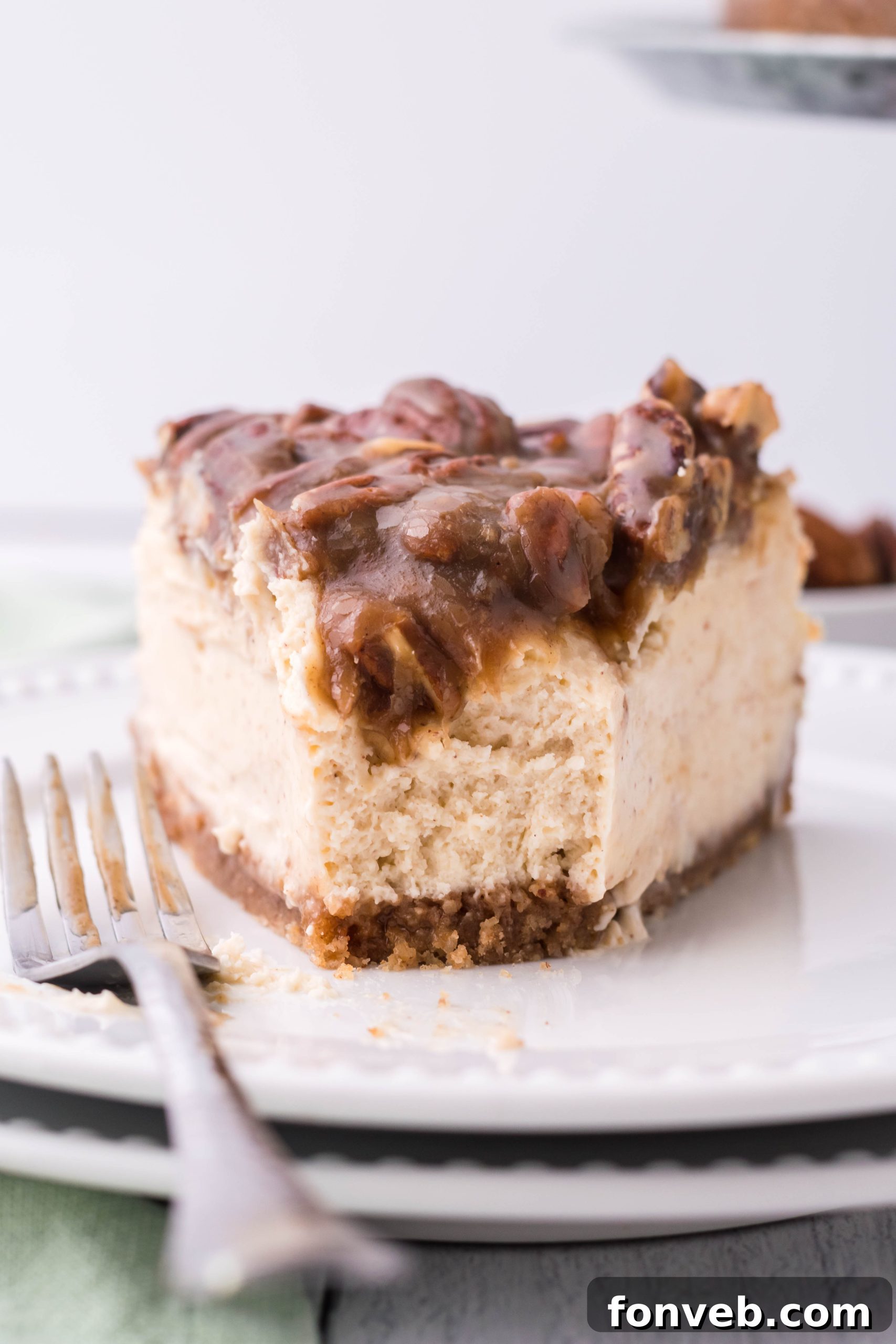 A delightful slice of Pecan Pie Cheesecake on a white plate with a small portion already enjoyed, indicating its irresistible nature.