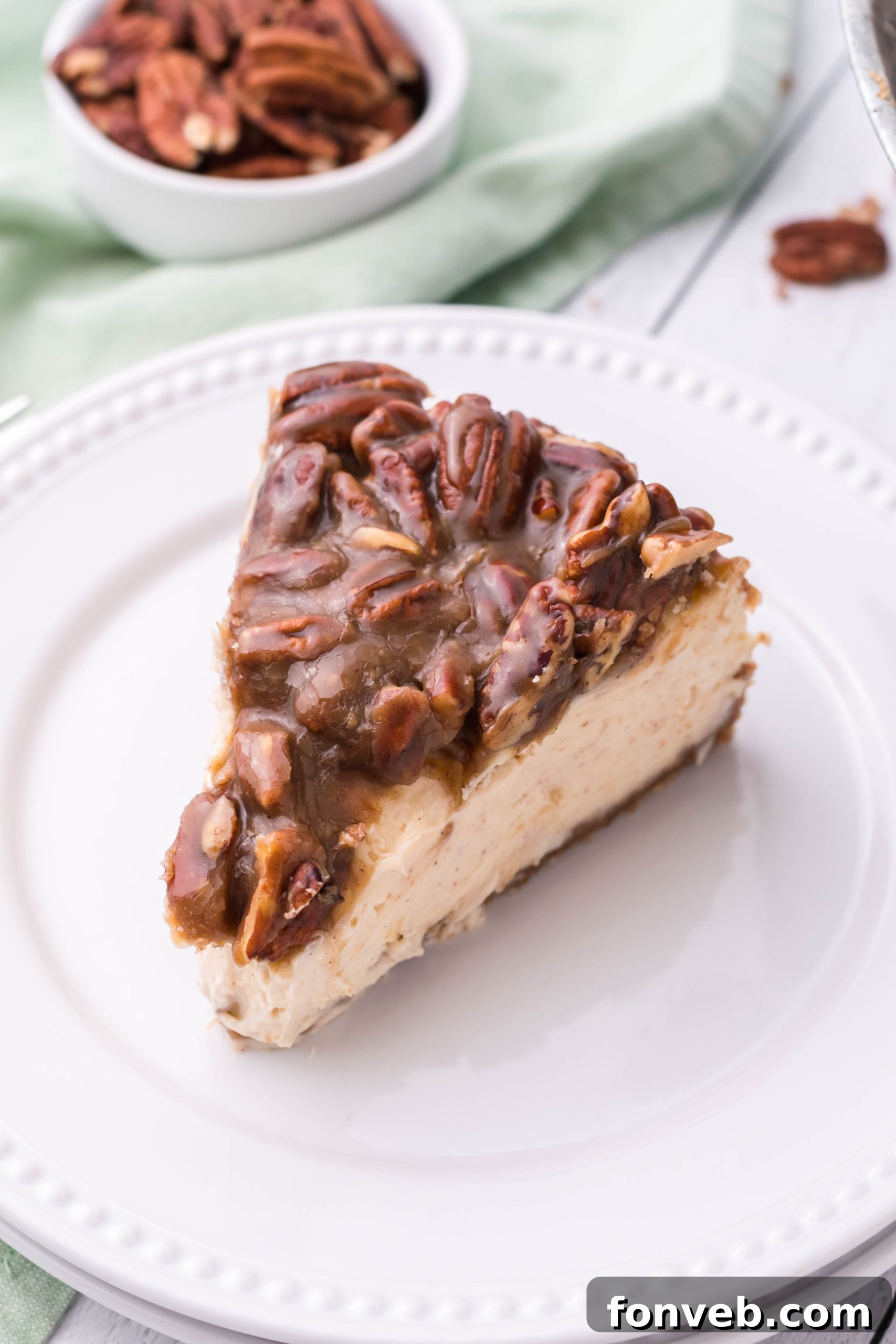 A pristine slice of Pecan Pie Cheesecake beautifully presented on a white plate, ready to be savored.