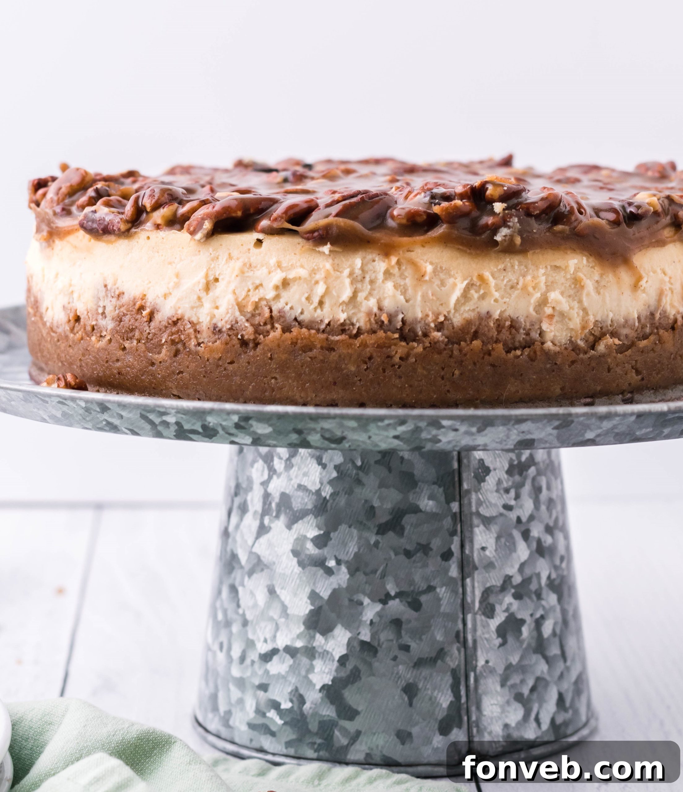 Pecan Pie Cheesecake presented beautifully on a elegant silver cake stand, viewed from a flattering side angle.