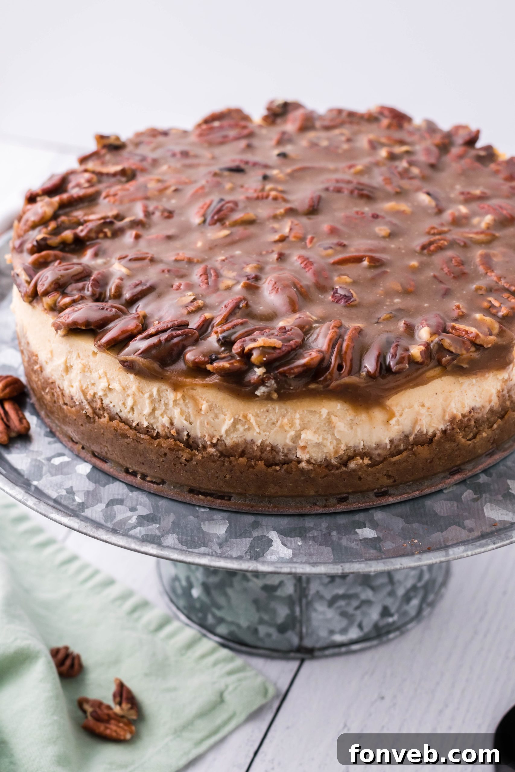 The full Pecan Pie Cheesecake, showcasing its impressive height and golden pecan topping, sits invitingly on a silver cake stand.