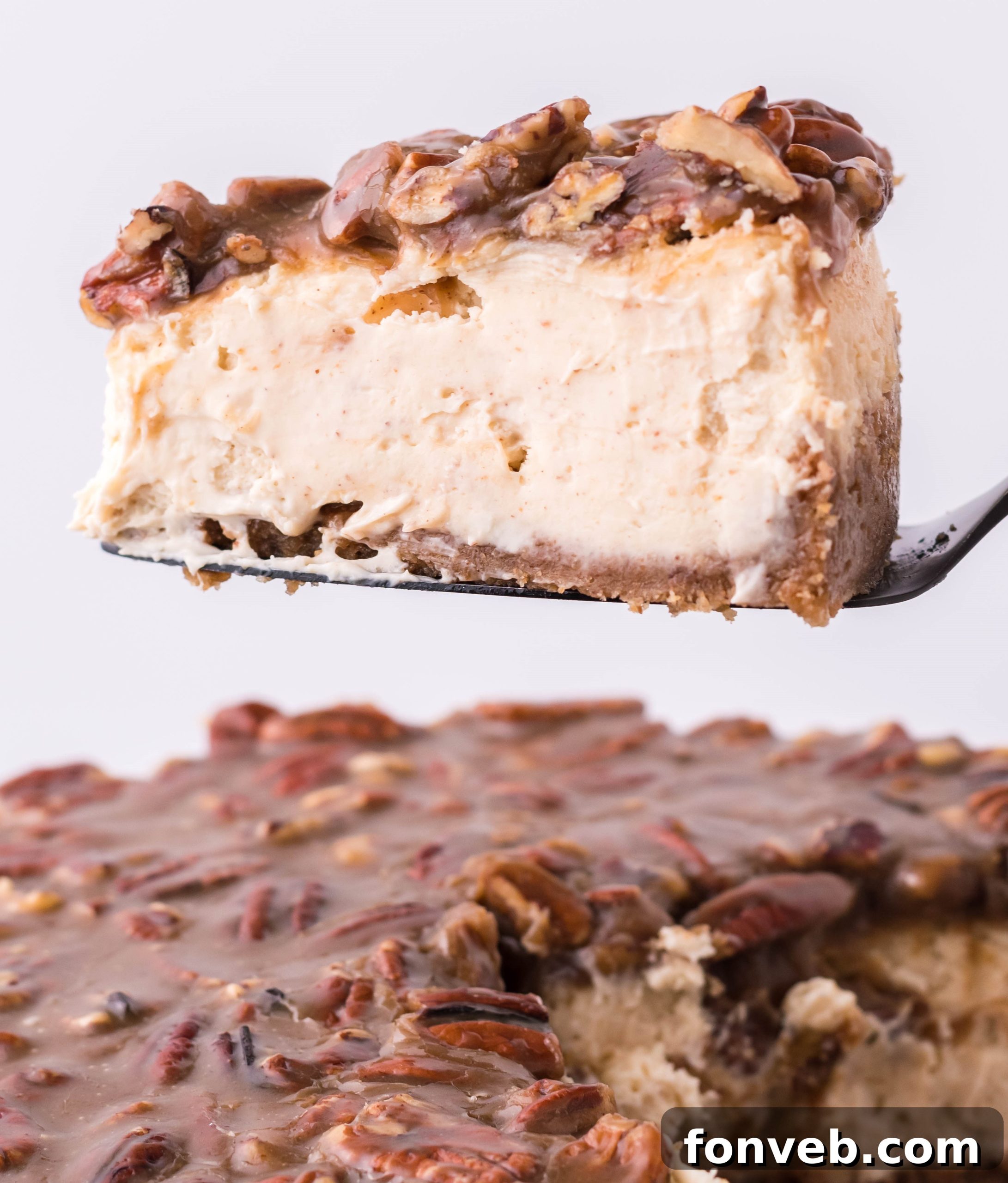 A perfect slice of Pecan Pie Cheesecake, showing off its layered perfection, is gently lifted by a cake server.