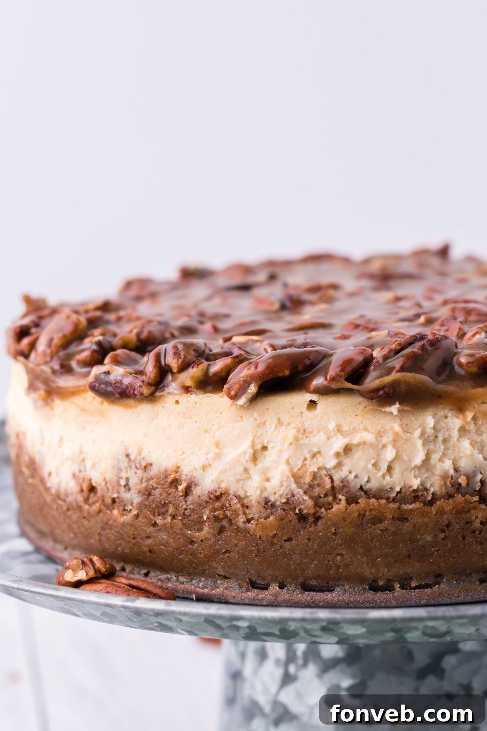 Pecan Pie Cheesecake displayed on a silver cake stand, captured from a different side angle, highlighting its golden crust.