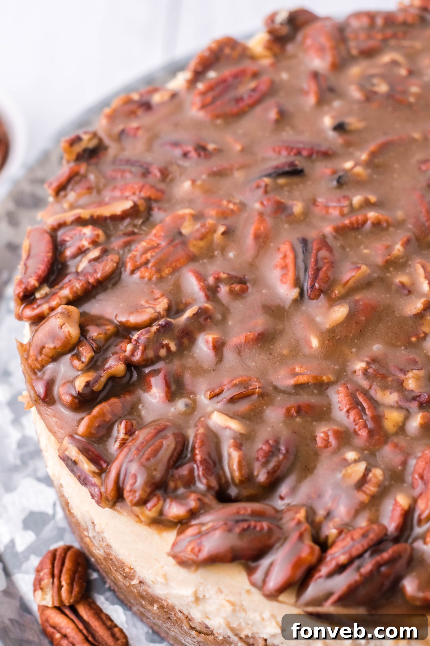 An overhead shot of the Pecan Pie Cheesecake on a silver cake stand, highlighting the generous pecan topping.
